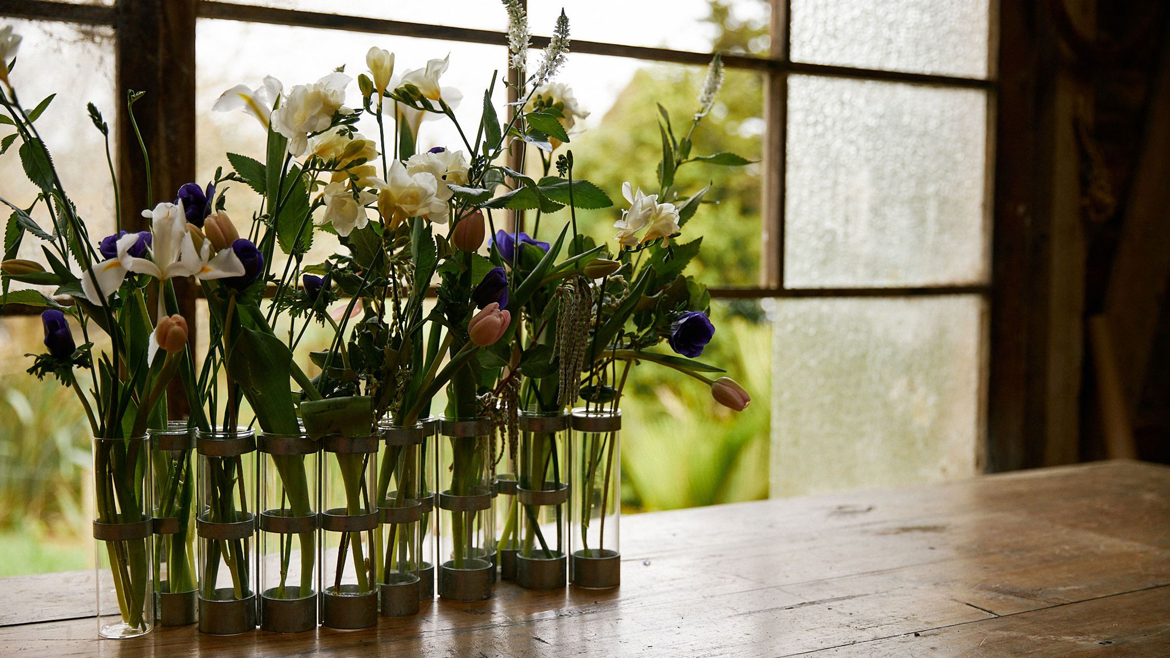 Wooden table with glass vase filled with spring blooms beside a window