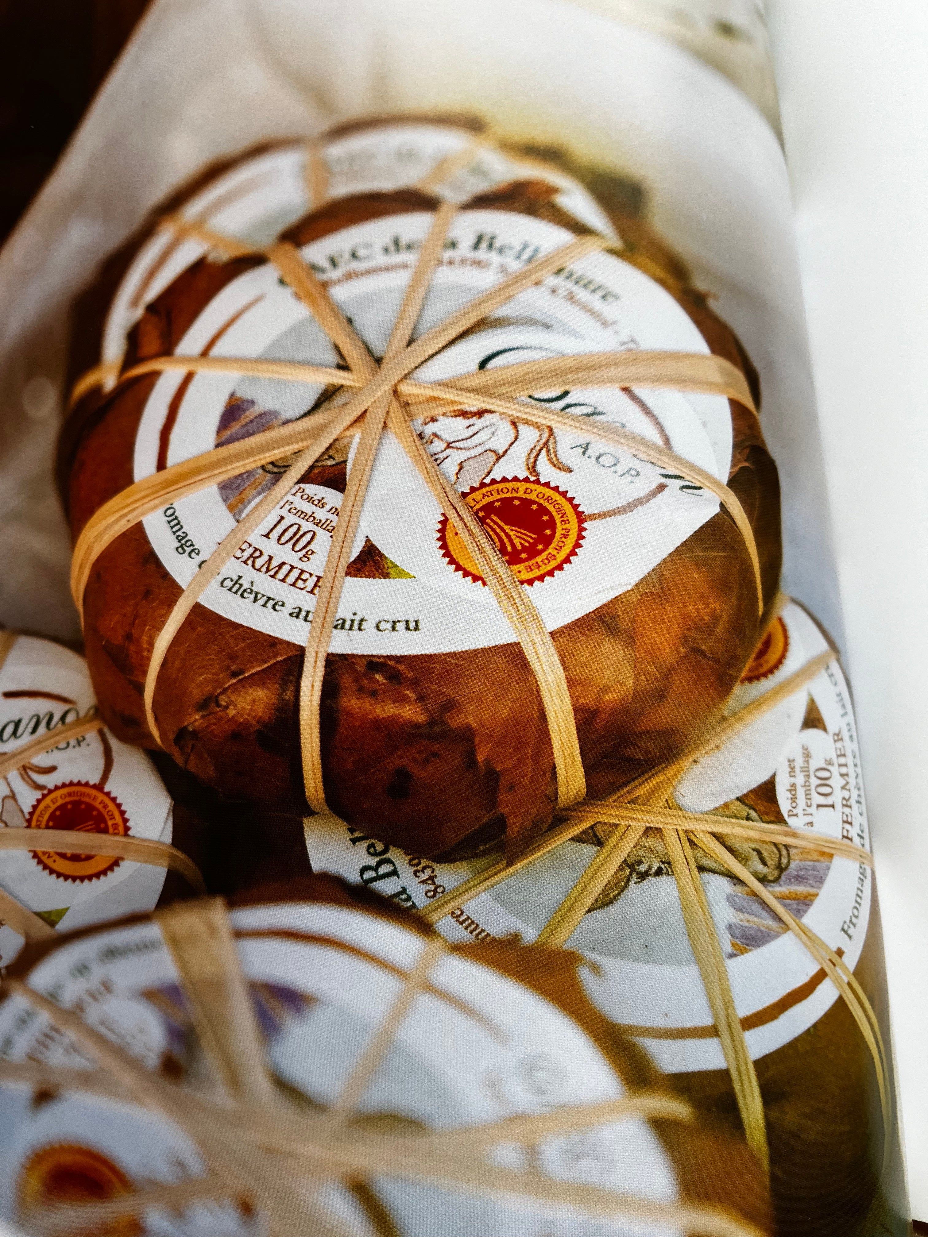 Stacked cheese packages wrapped in brown paper with rubber bands. White labels indicate goat's milk cheese.