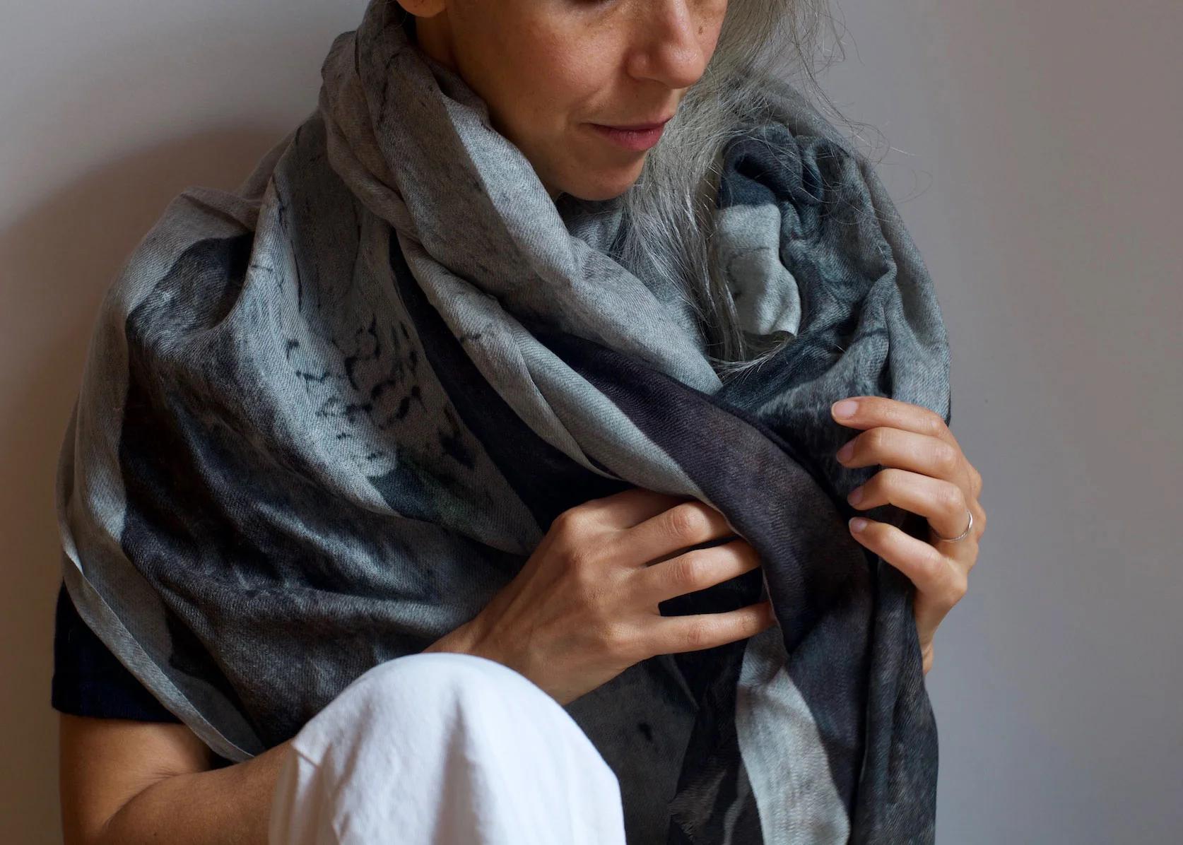 Person wrapping multi-tone Good & Co scarf around shoulders. Wearing black top and white pants. Simple background emphasises loungewear.