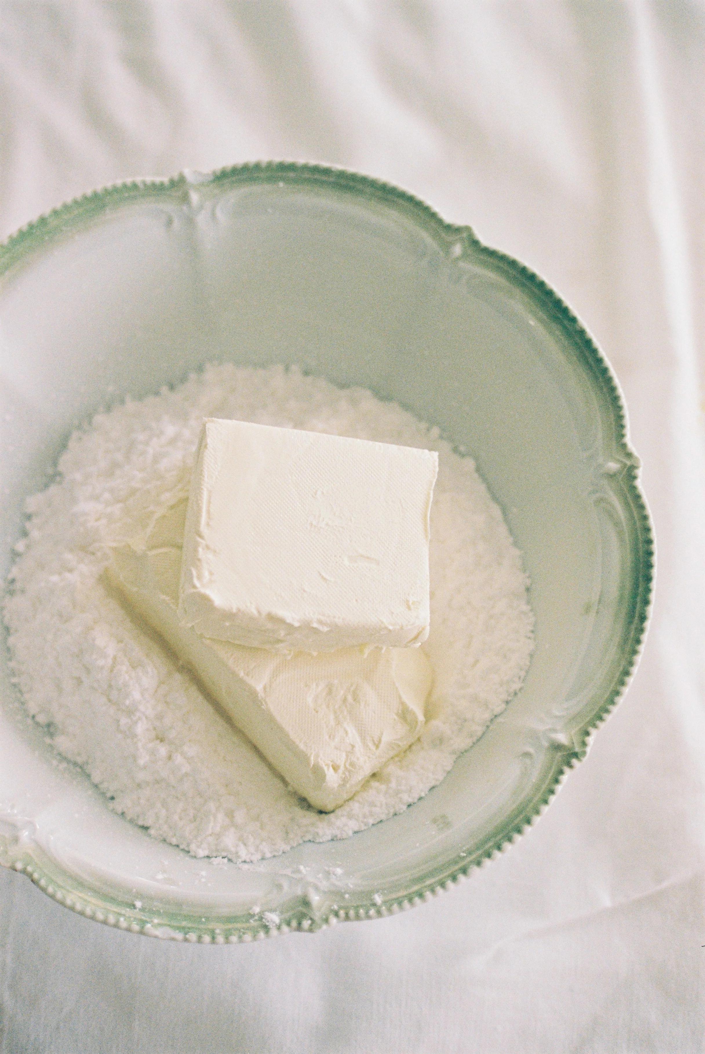 Vintage bowl with butter blocks on confectioner's sugar. Green-edged white ceramic. Softly lit white cloth.