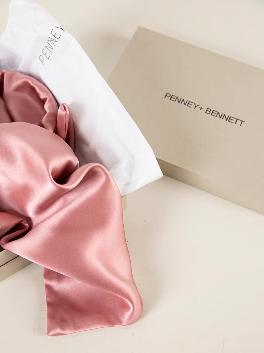 Open Penney+Bennett box with pink silky fabric spilling out. White paper lining visible. Placed on neutral-coloured surface.