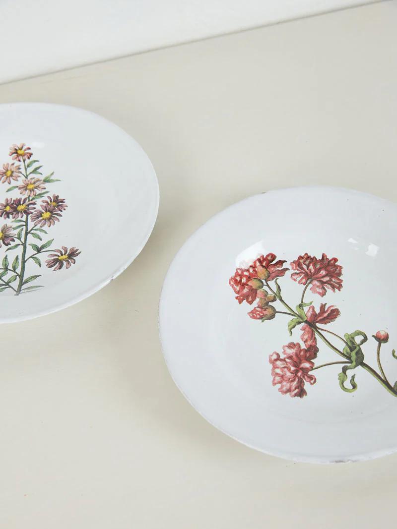 Two white plates with floral designs. Left plate has purple and yellow flowers, right has pink and red blossoms.