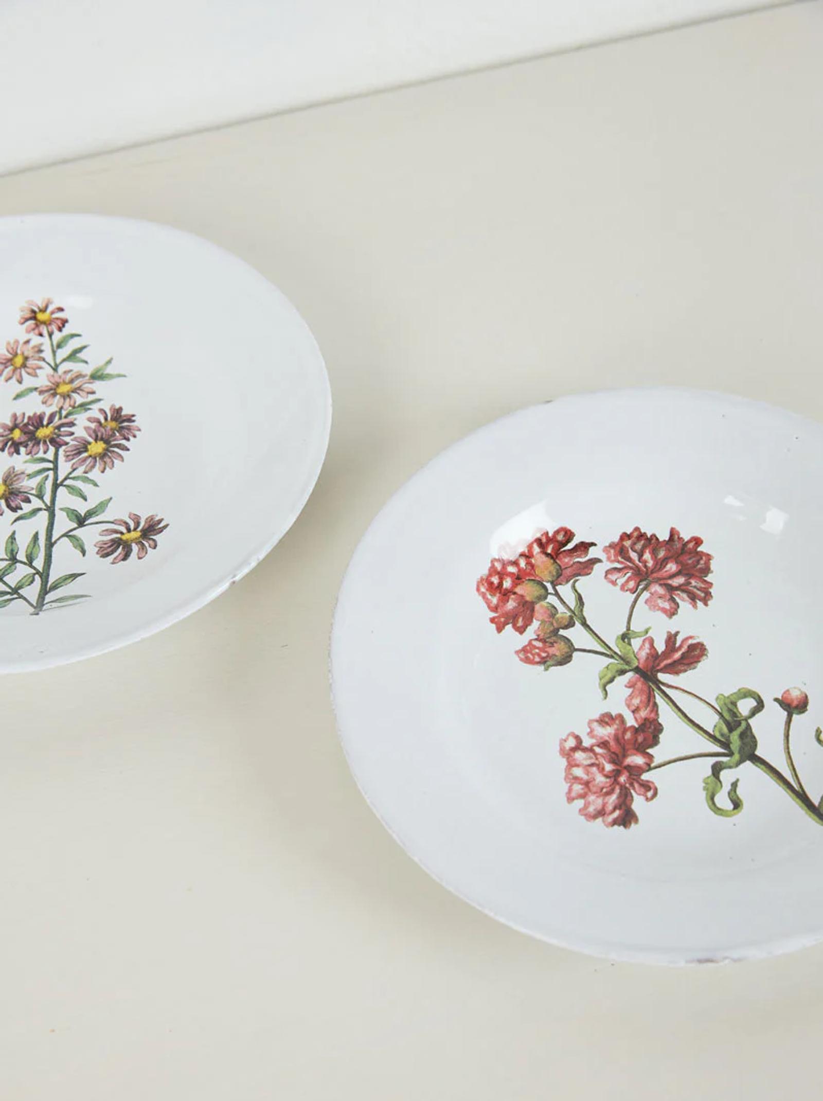 Two white plates with floral designs. Left plate has purple and yellow flowers, right has pink and red blossoms.