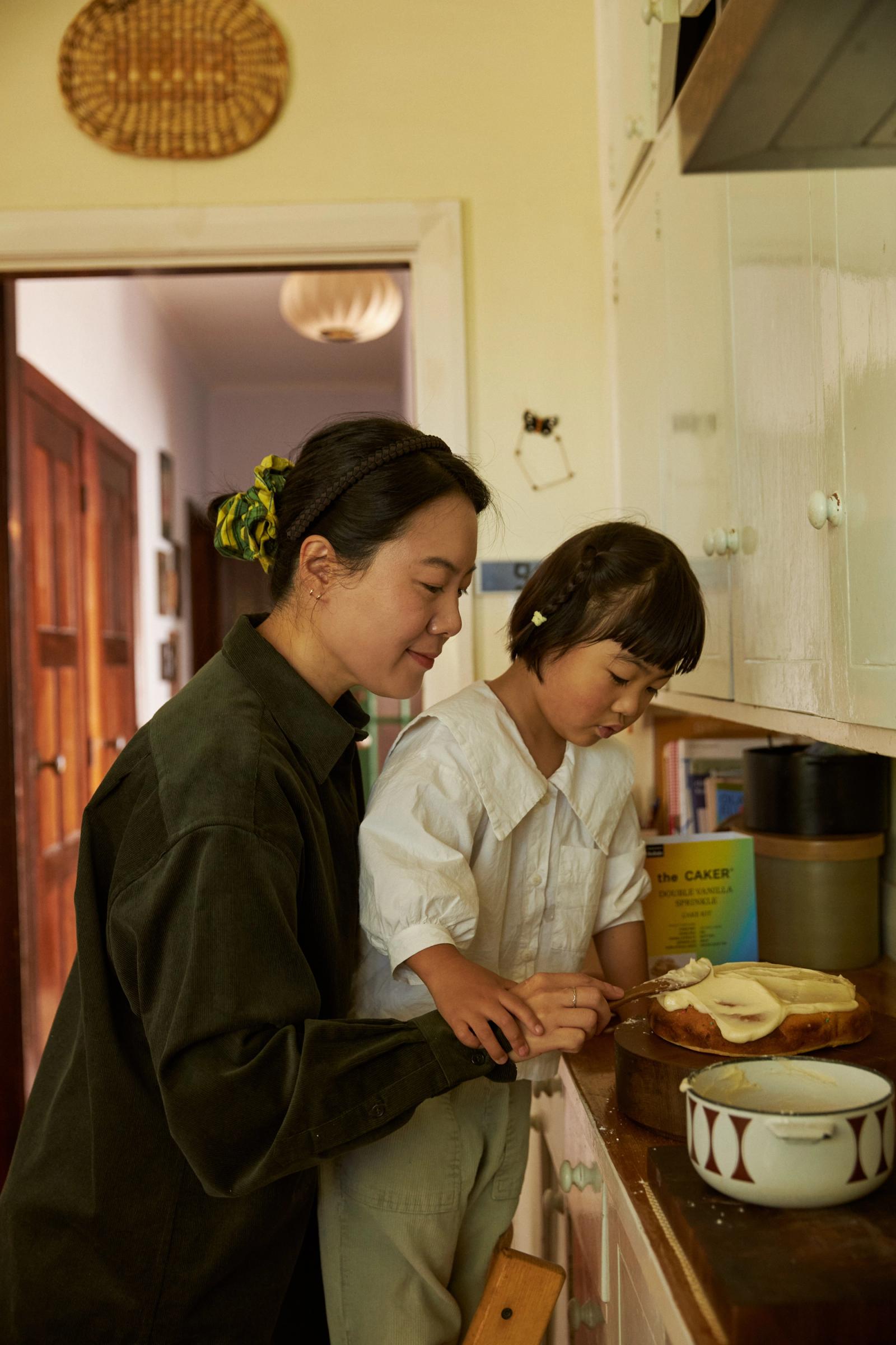 Jiho and Eden stand at the kitchen bench and ice the cake