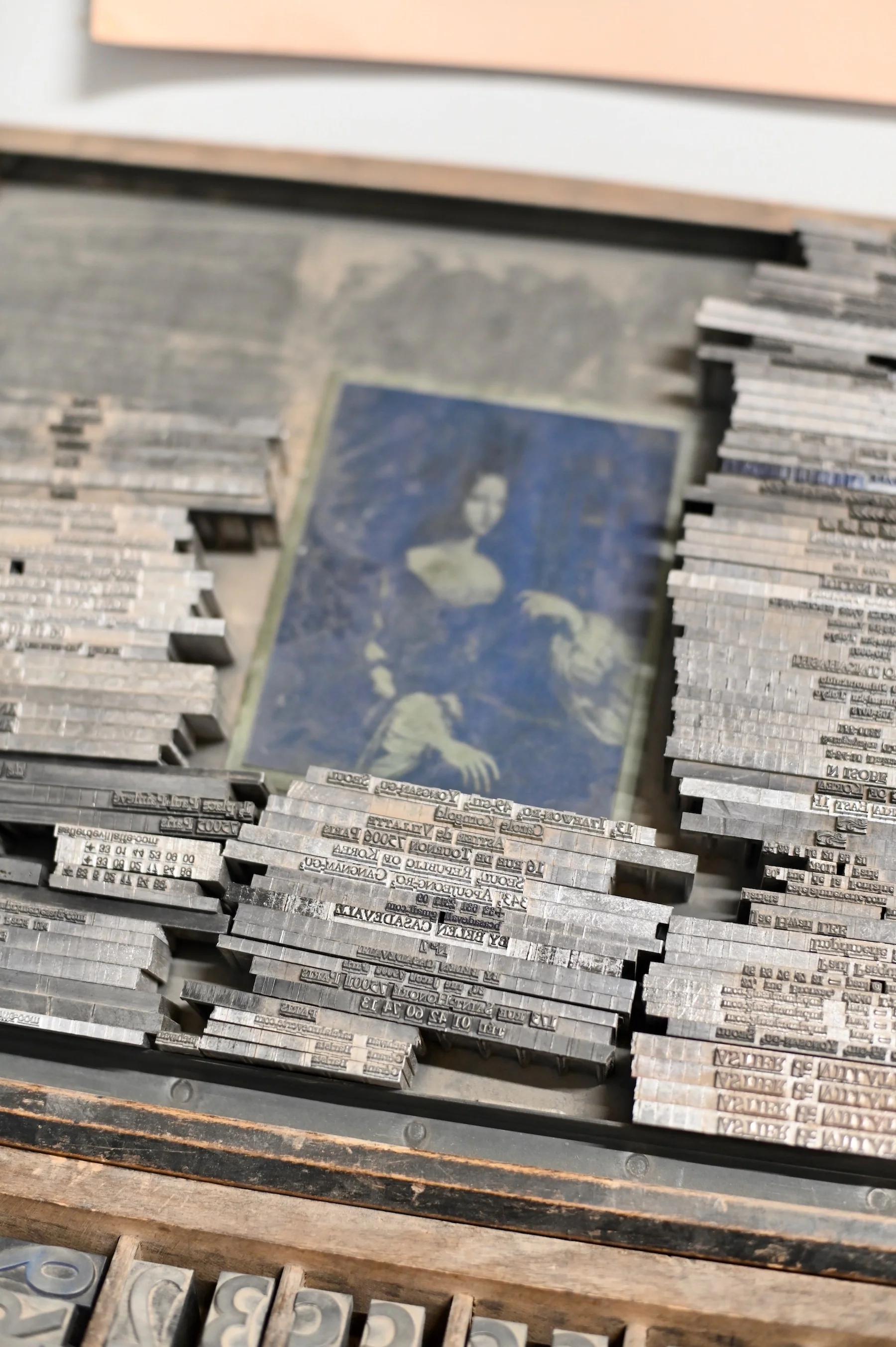 Vintage printing blocks arranged in rows on wooden tray. Faded photograph of woman in formal dress in center.