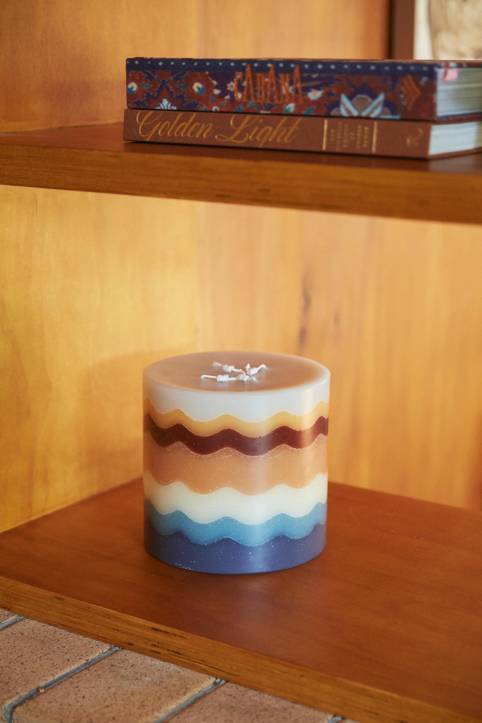 Striped candle on wooden shelf. "CABANA" and "Golden Light" books above. Wooden panel wall background.