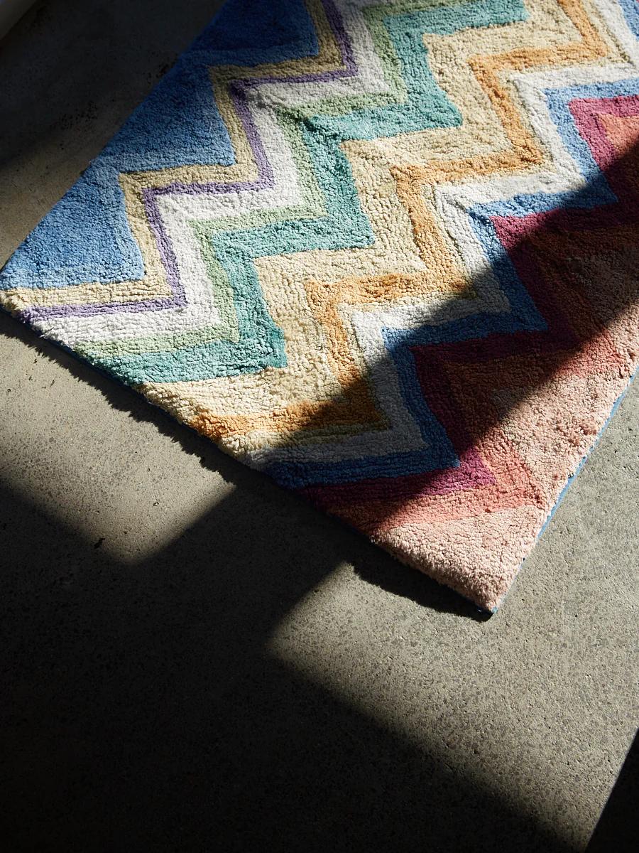 A colourful zigzag rug on a concrete floor, with sunlight and shadows from window frames.