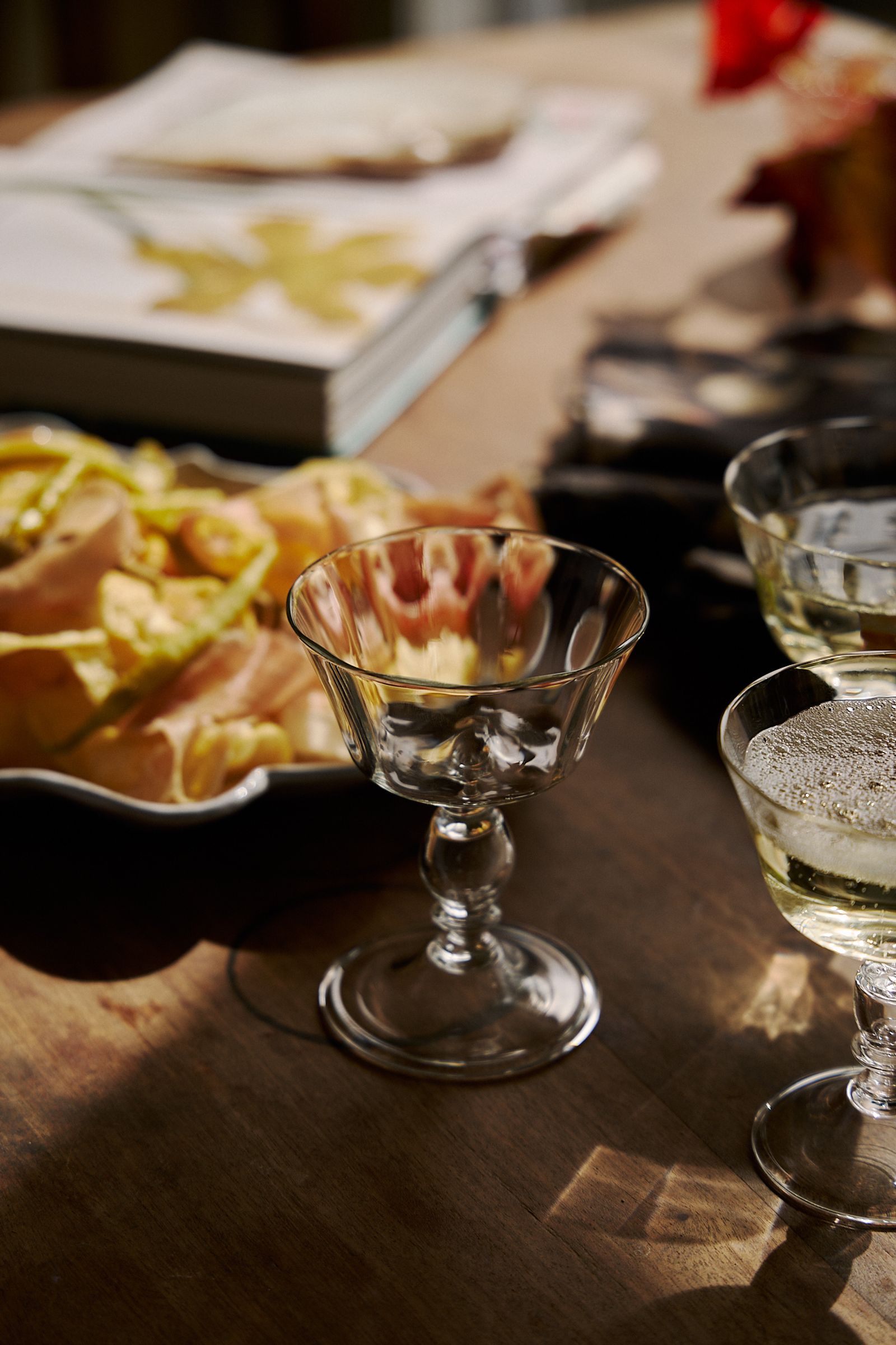 champagne glass sits in sunlight on table next to a book and platter