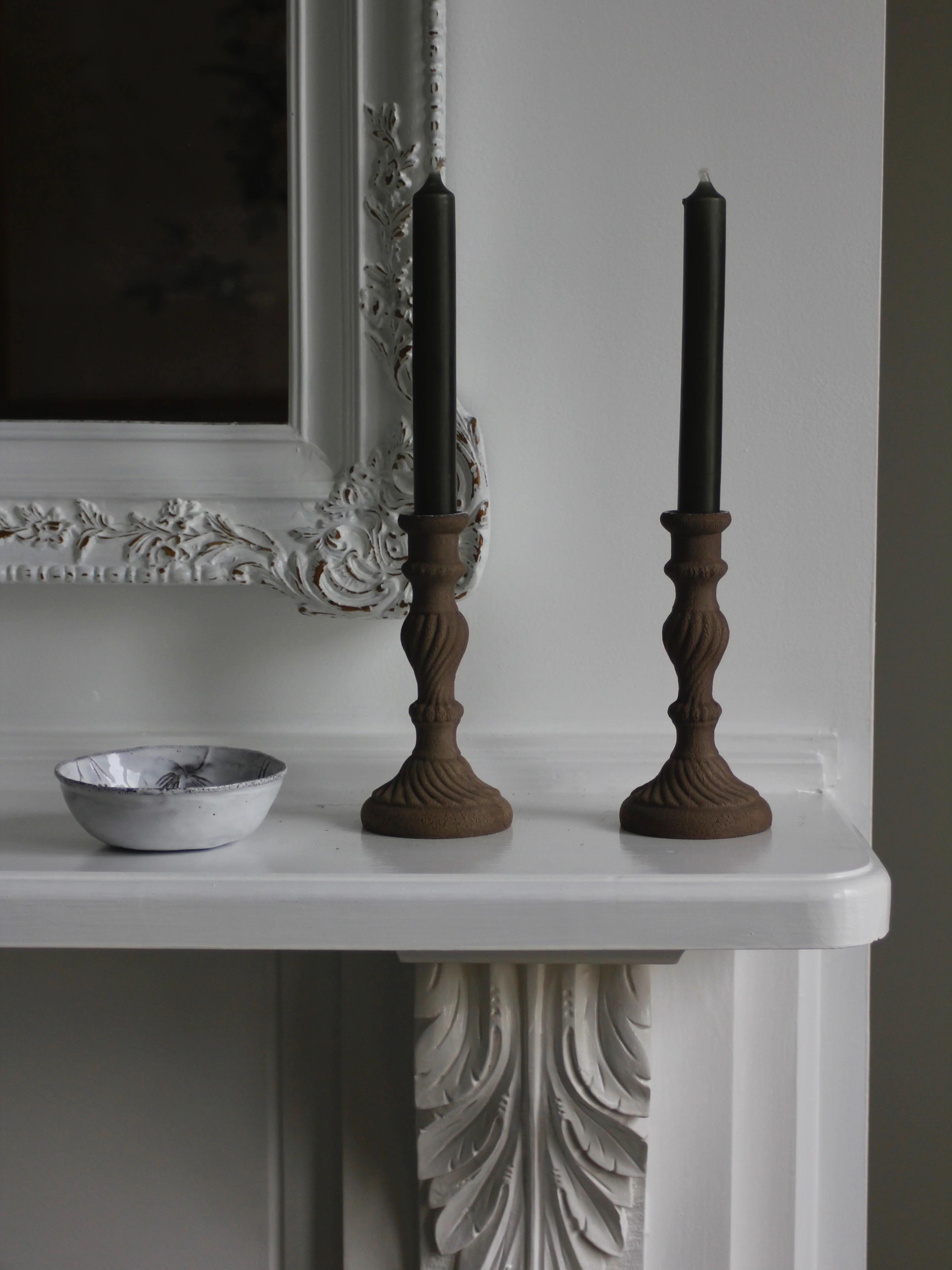 White mantel with intricate black candlesticks. Small patterned bowl in Astier de Villatte style. Embellished moulding creates wintry atmosphere.