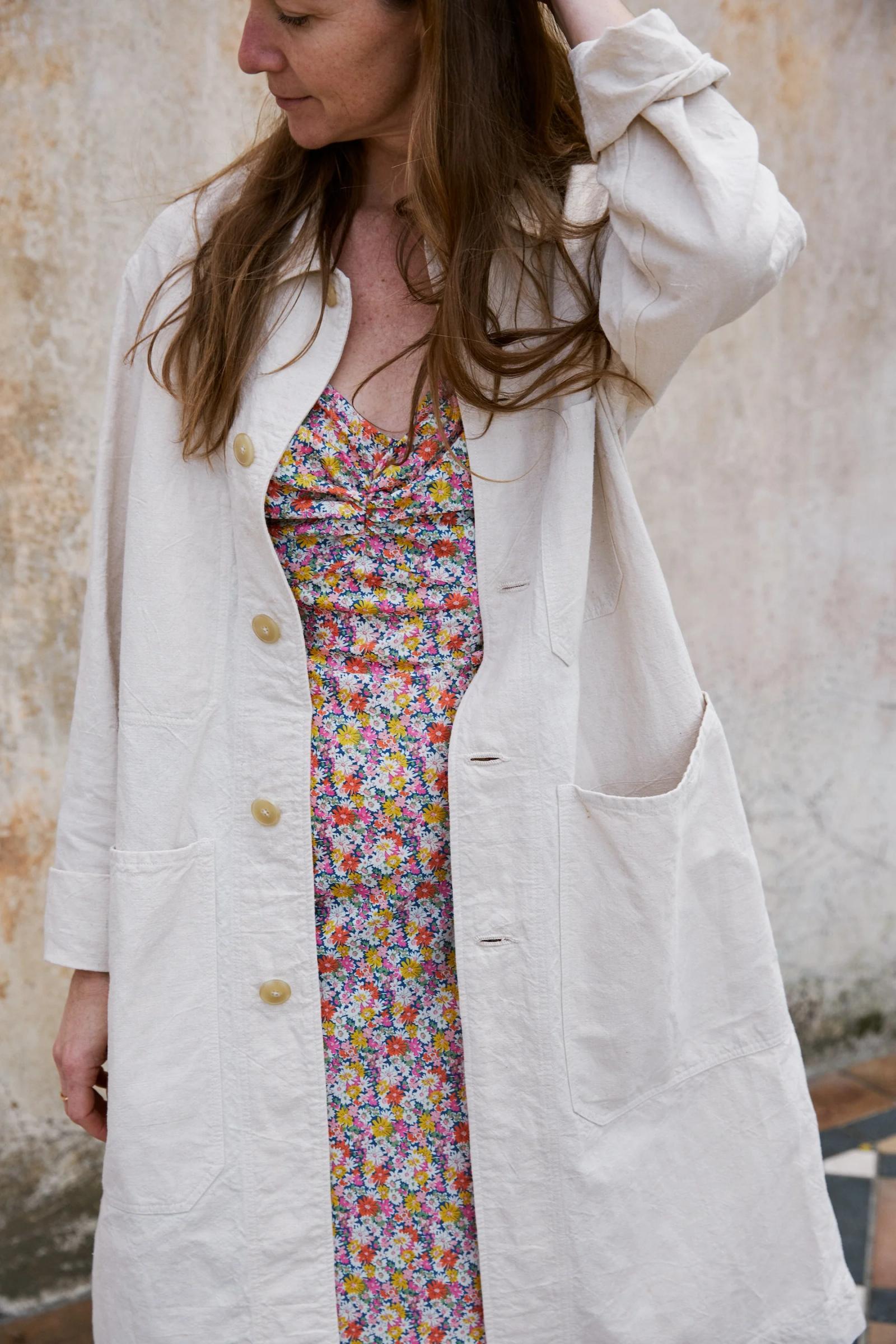 Long cream cotton coat, worn open over a floral dress.