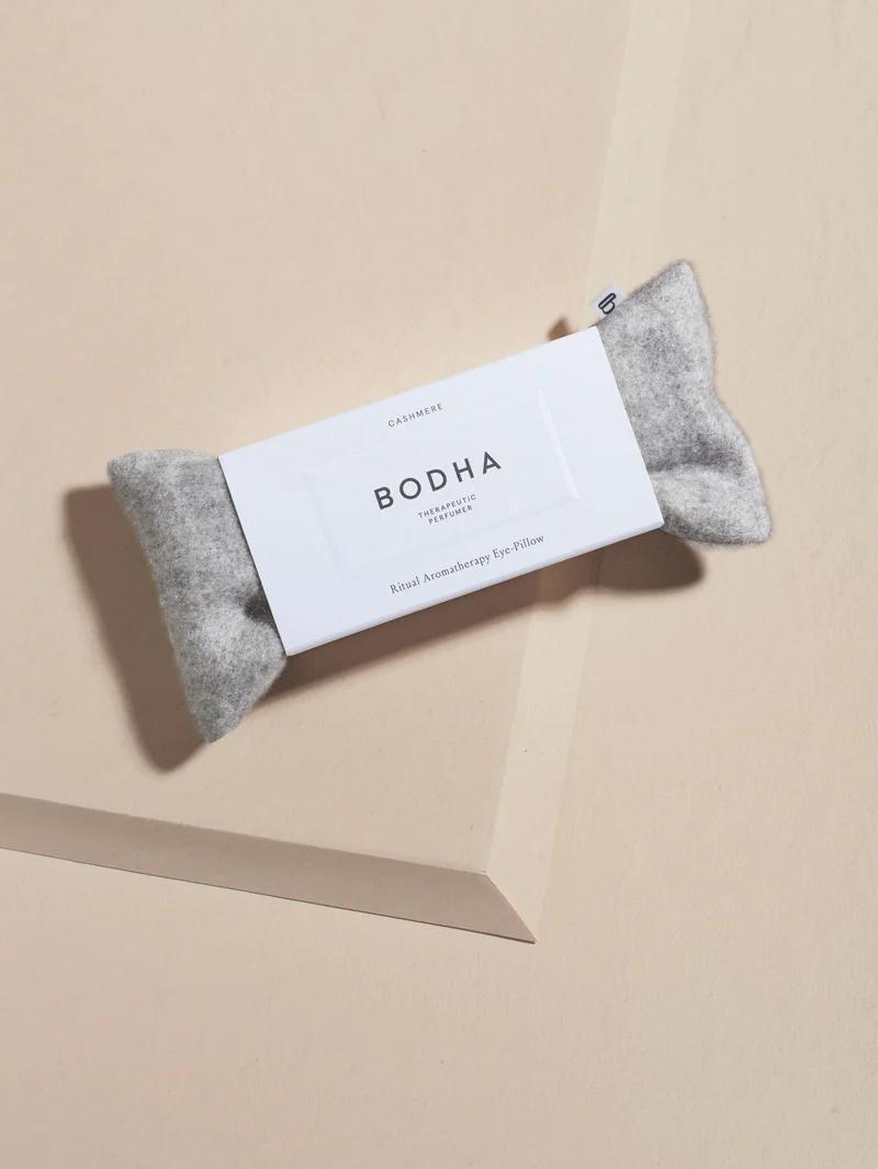 A grey BODHA eye pillow with a white label reading “Ritual Aromatherapy Eye Pillow” against a light, neutral background.