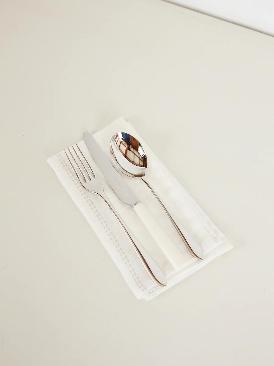 Fork, knife, and spoon on white napkin. Utensils aligned parallel, fork left, knife middle, spoon right.