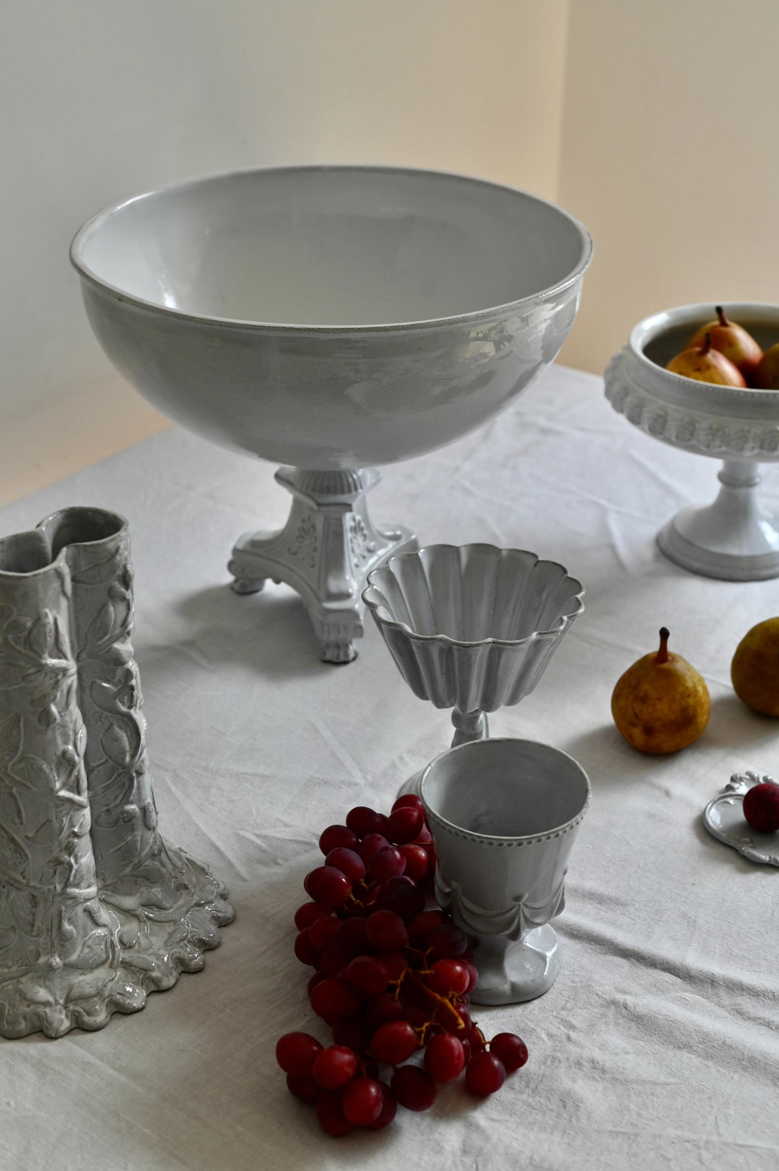 a group of Astier de Villatte ceramics on a table with white cloth in natural light