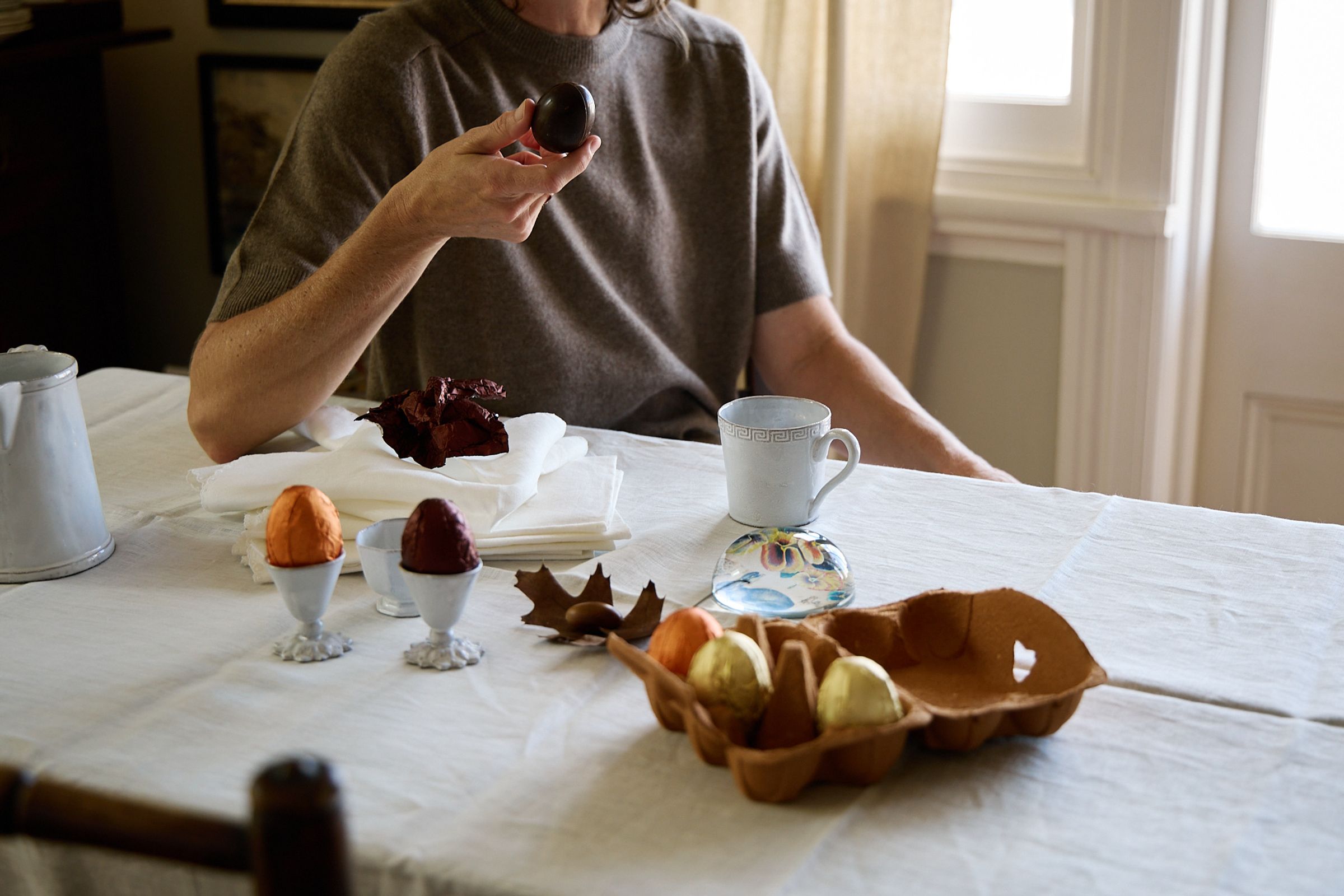 dining table in white cloth with woman holding easter eggs and coffee