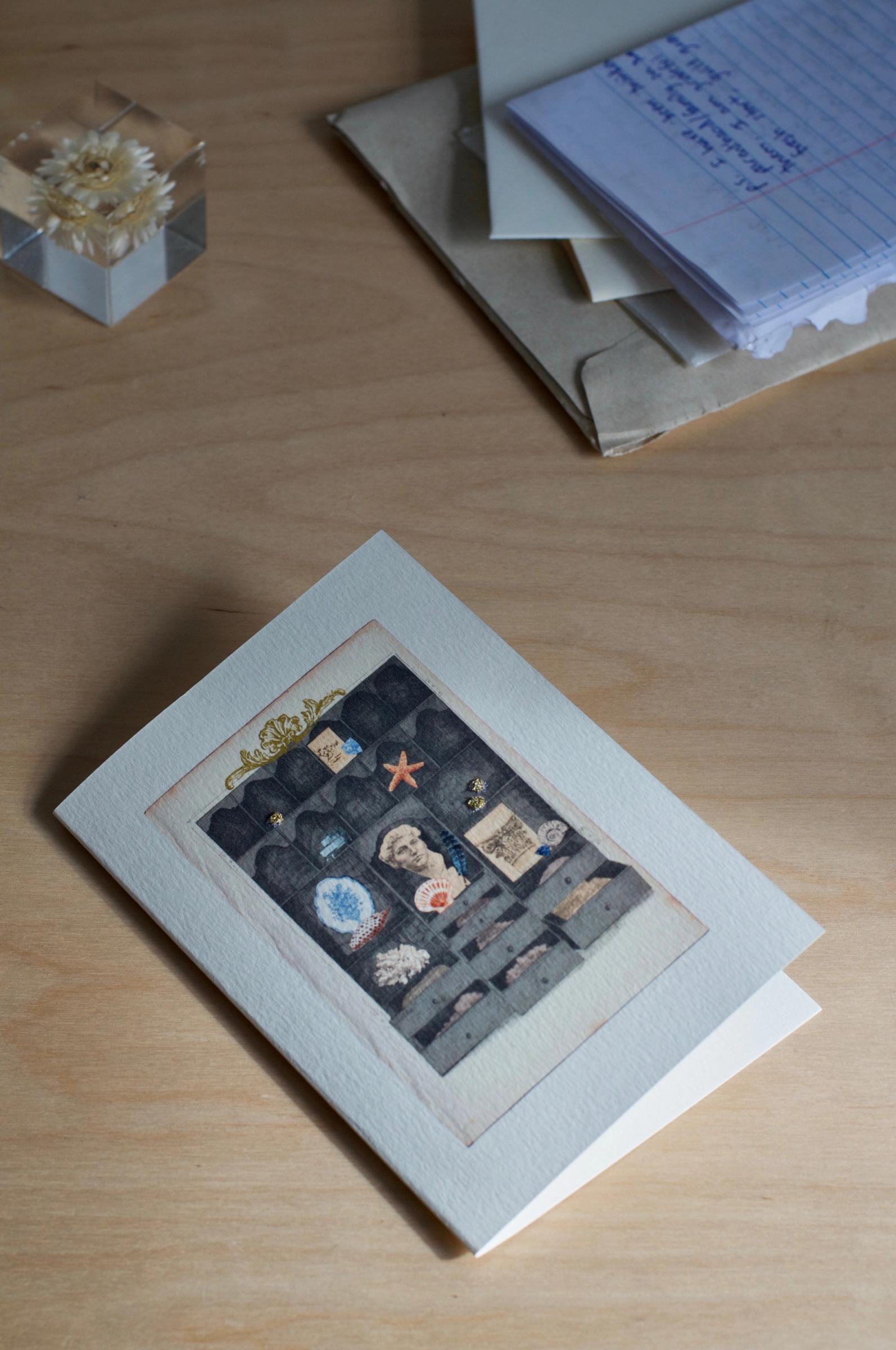 A greeting card with a display cabinet illustration, filled with various small items. The card stands against a plain white background.