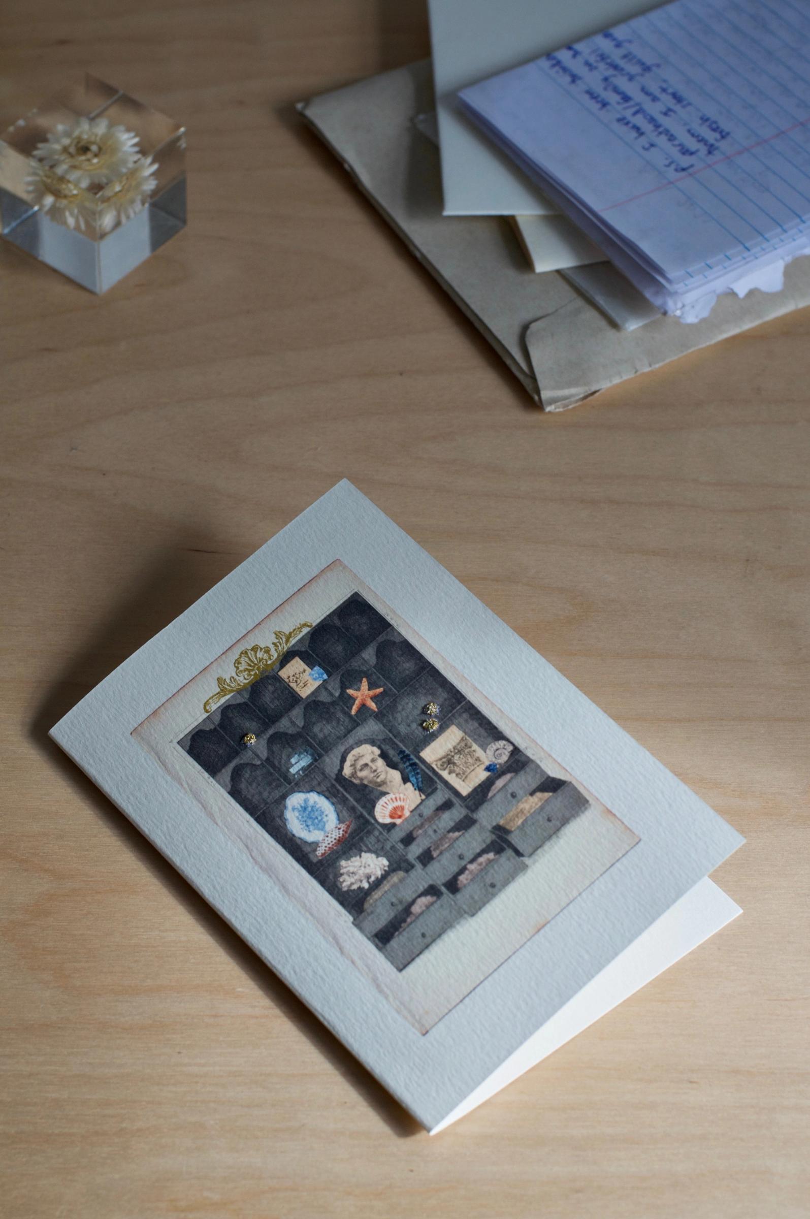 A greeting card with a display cabinet illustration, filled with various small items. The card stands against a plain white background.