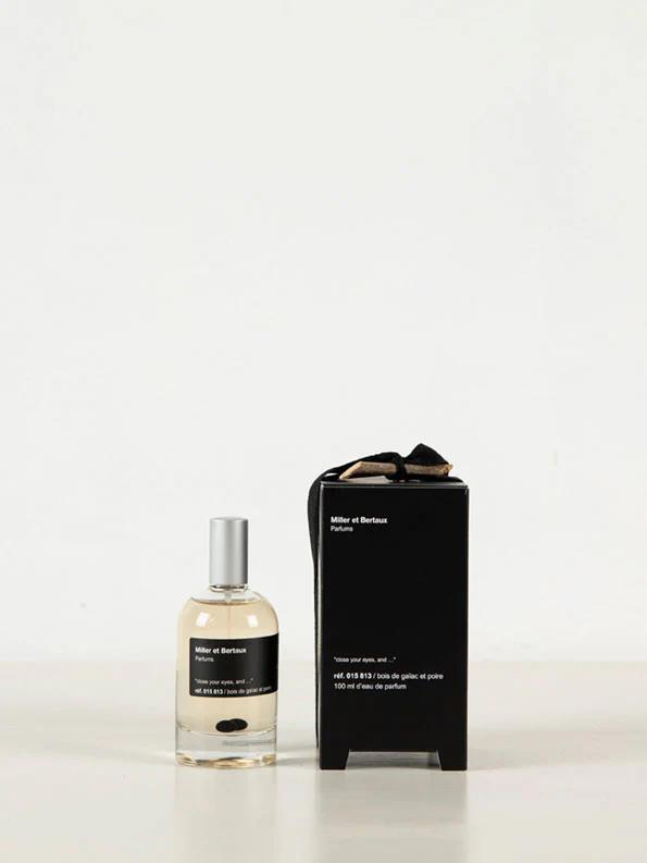 Elegant perfume display: Clear glass bottle with black label beside matching box. Silver cap and light-coloured liquid. Box features white text and black ribbon, evoking Miller et Bertaux's Parisian style.