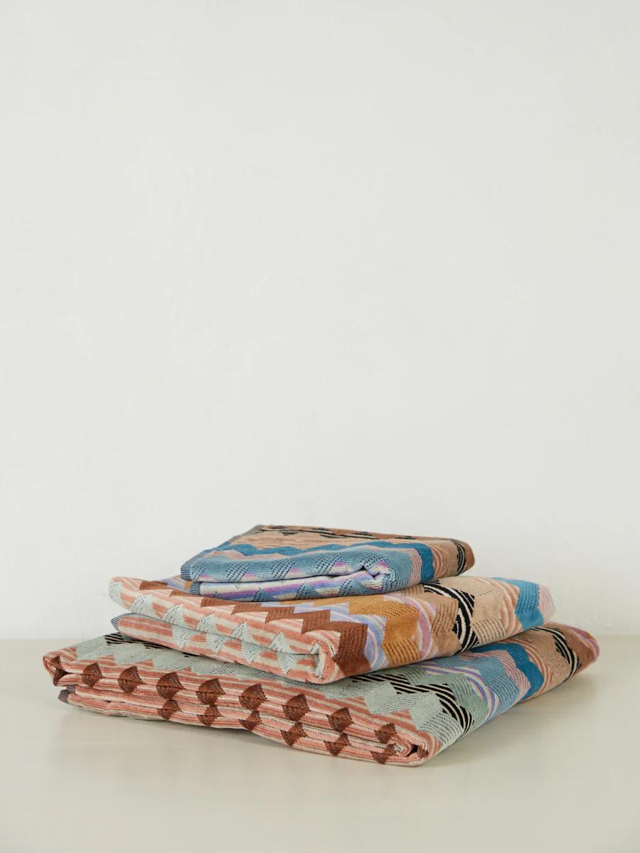 Three folded towels with geometric patterns in brown, blue, pink, and green from the Missoni collection, stacked on a white surface.