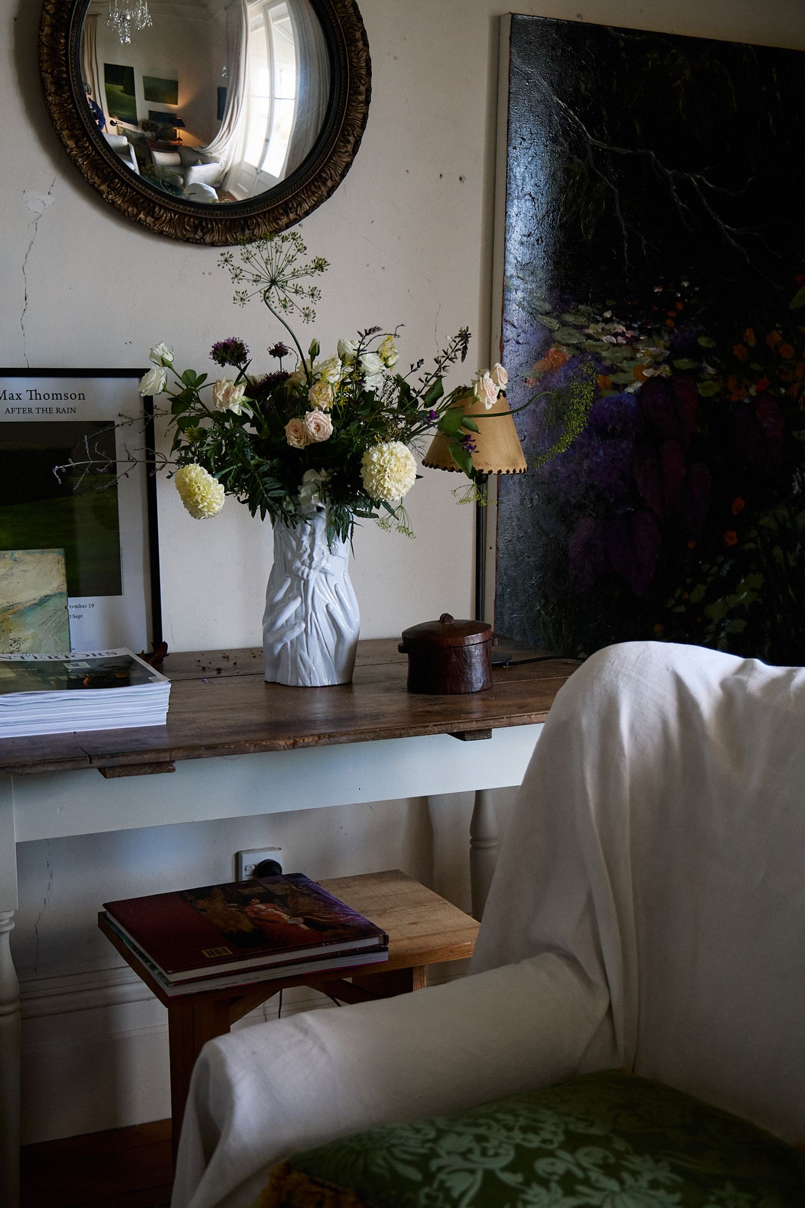 a white ceramic vase sits on an antique table next to a lamp and a painting