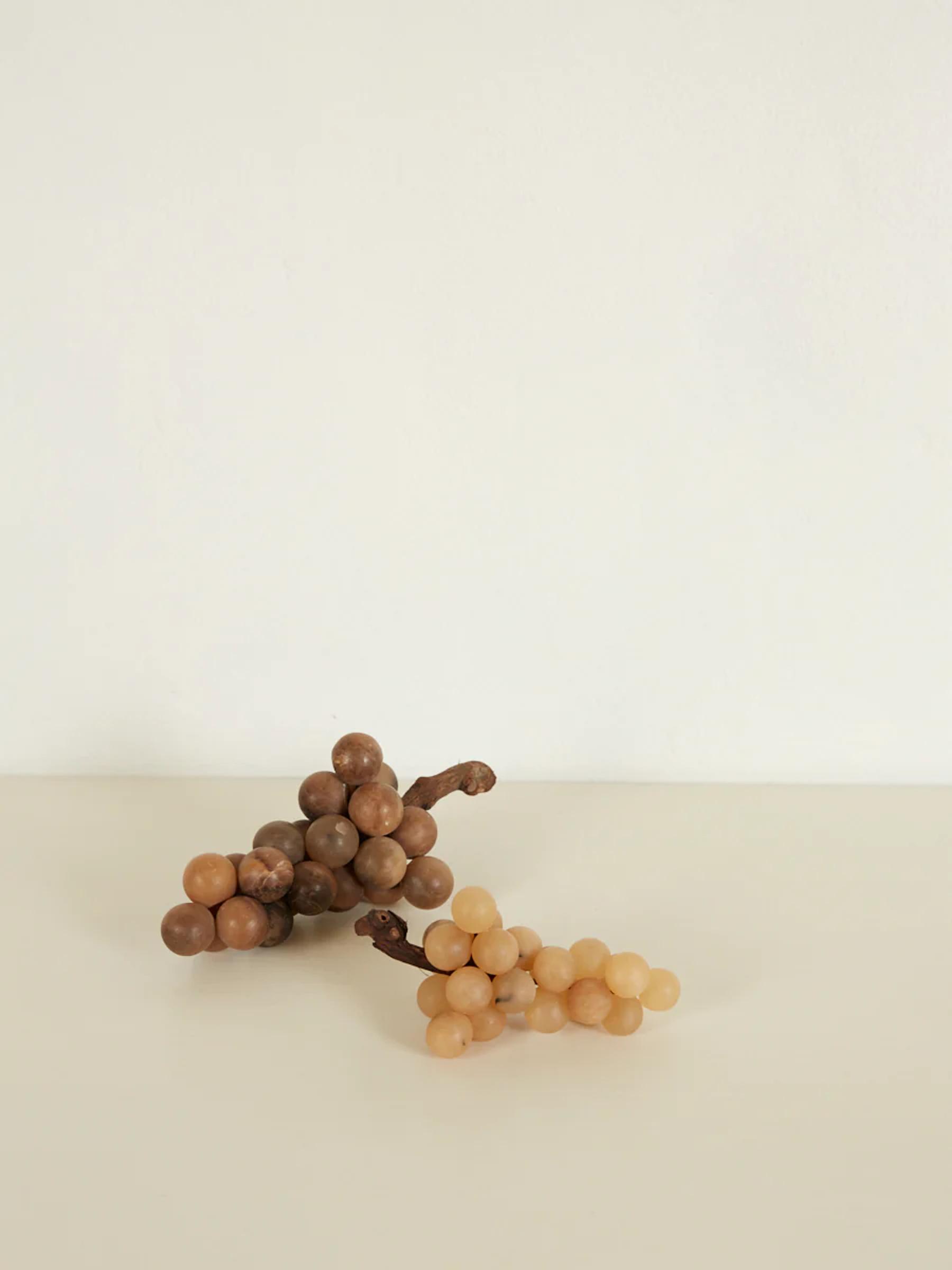 Two clusters of beige and brown grapes on light Carrara marble surface. White background creates minimalist, serene atmosphere.