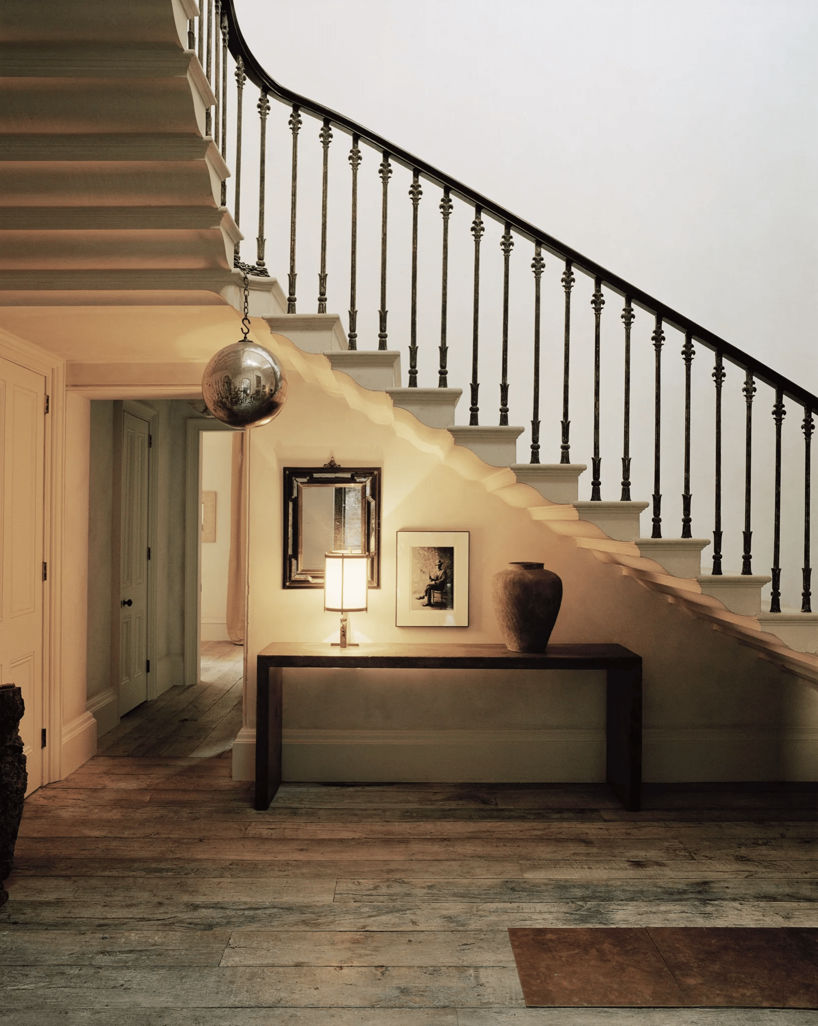 Modern staircase with black railing and light steps. Console table below holds lamp, art, and vase.