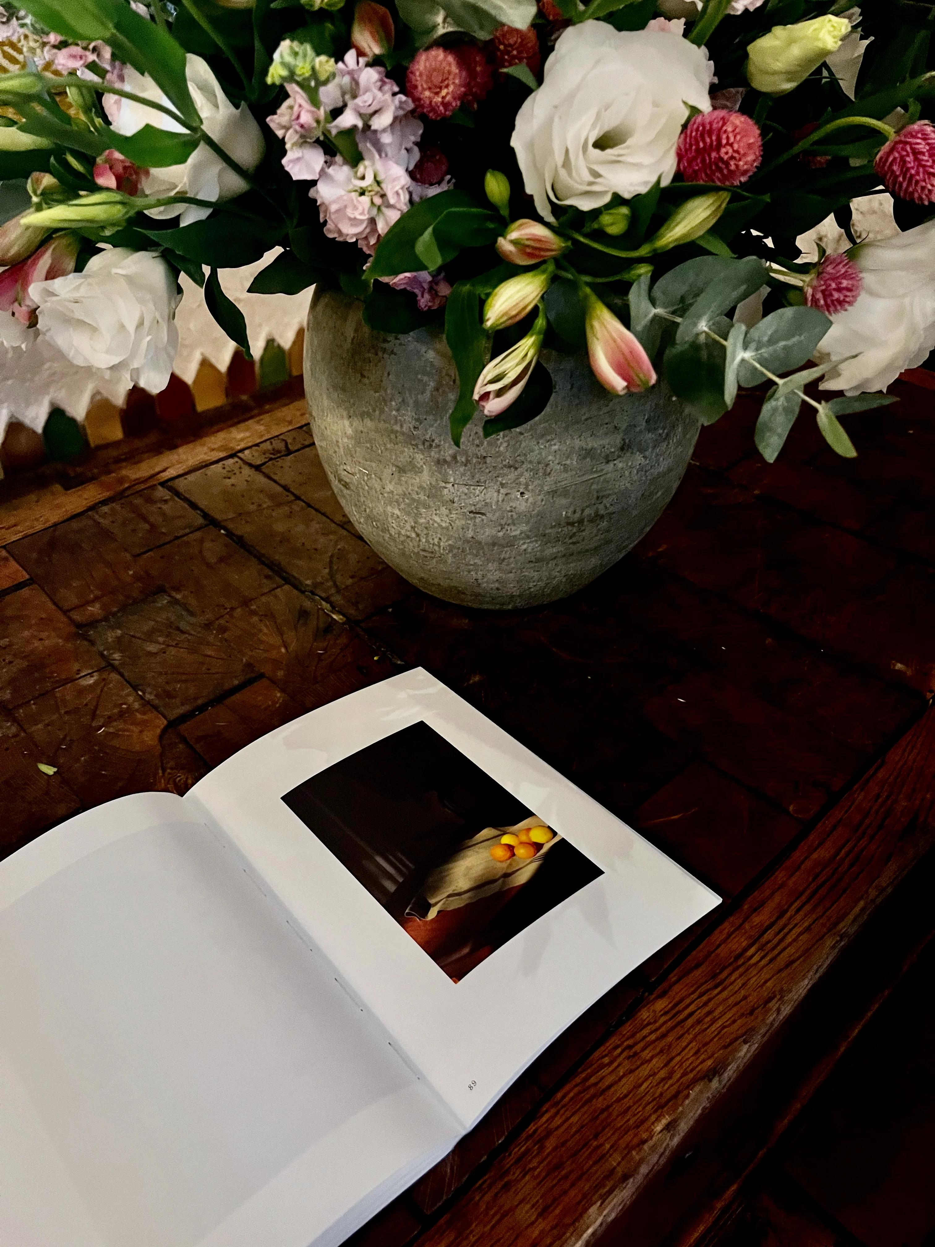 Rustic vase with colourful flowers on wooden table. Open book with bird photo in front.