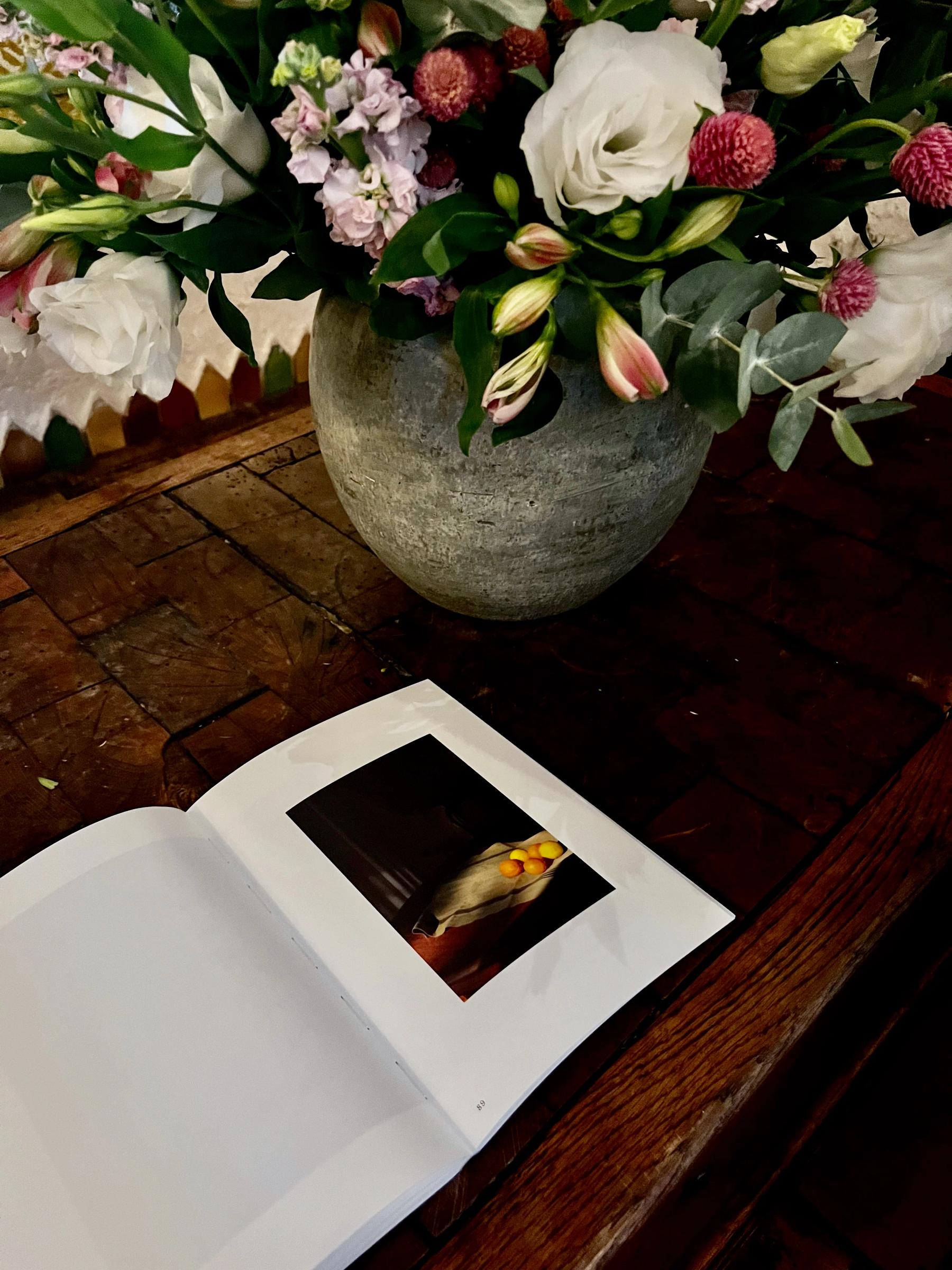 Rustic vase with colourful flowers on wooden table. Open book with bird photo in front.