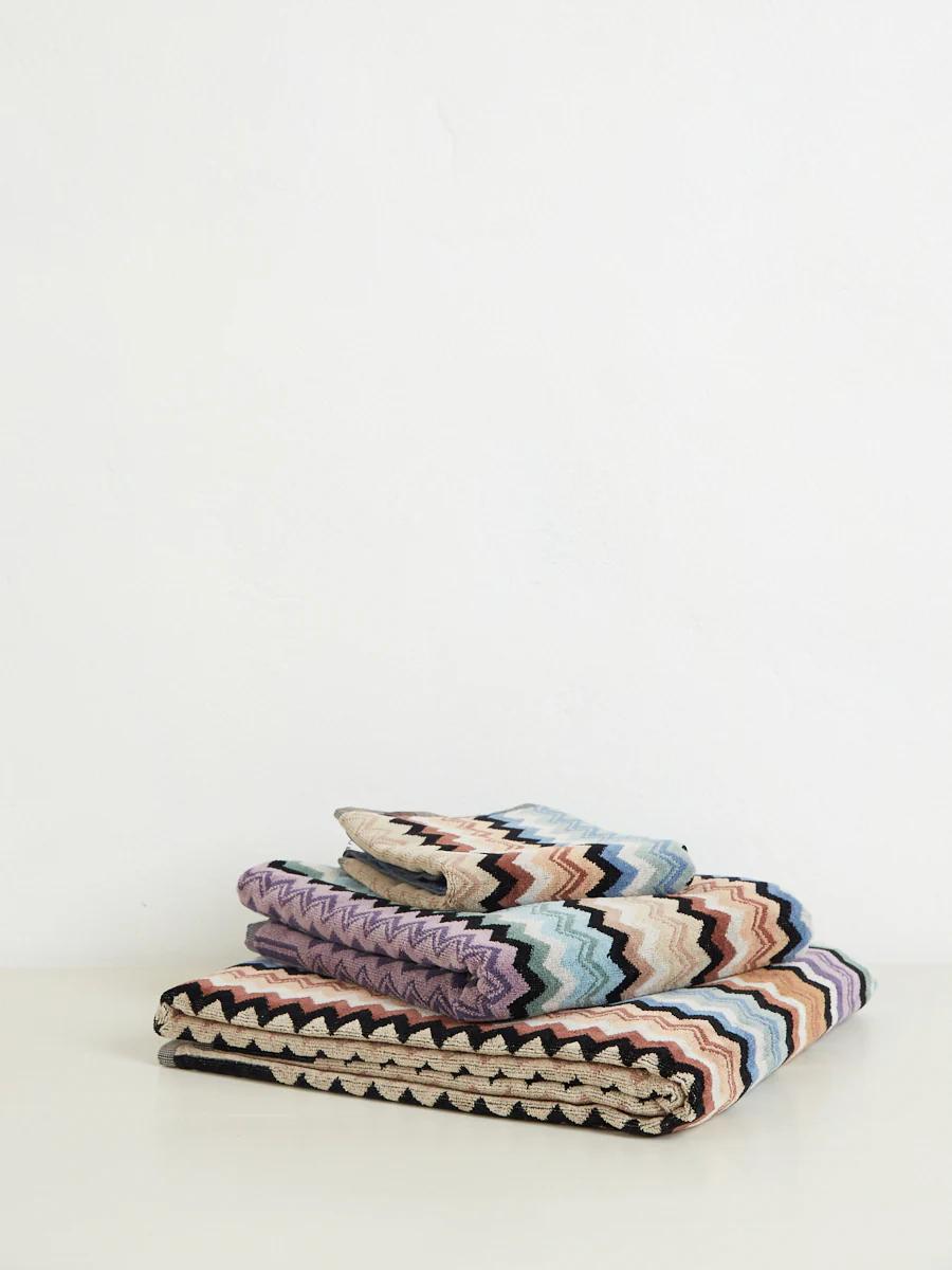 Three folded towels with zigzag patterns in purple, blue, brown, black, and white, stacked on a white surface.