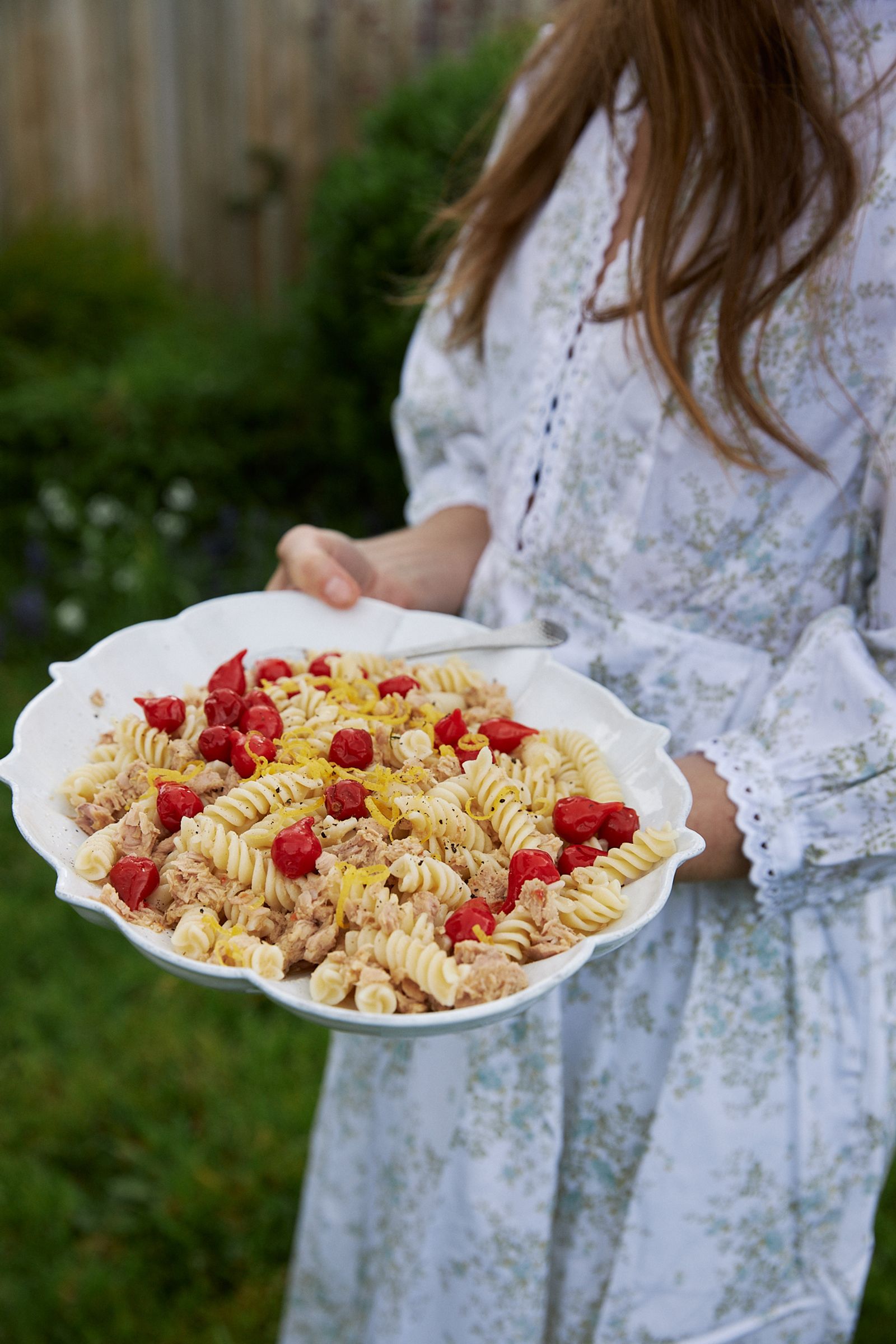 woman carries a platter of salad across the garden to the table