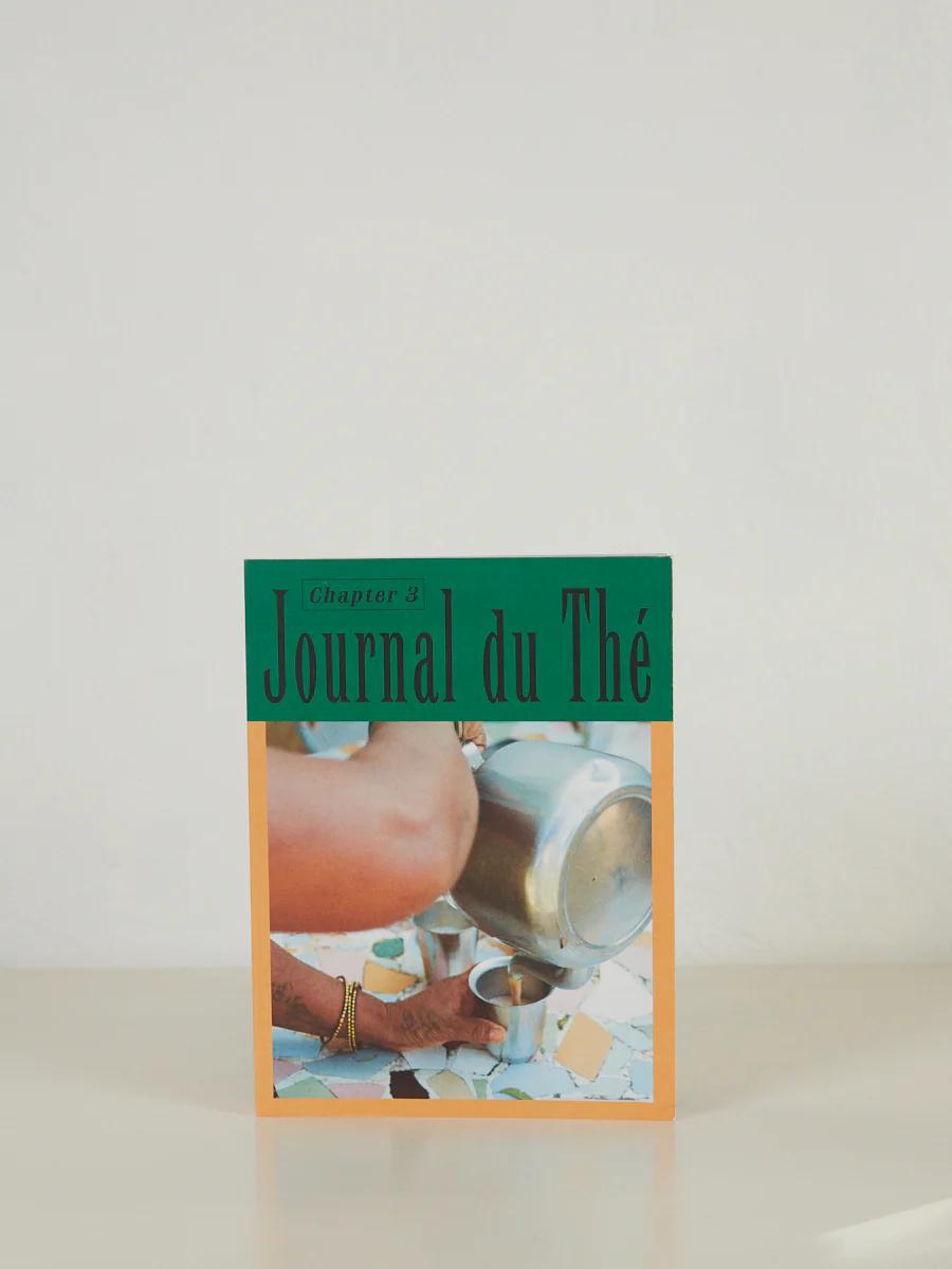 Colorful "Journal du Thé" book cover. Image of hands pouring tea below title. Green background, orange border.