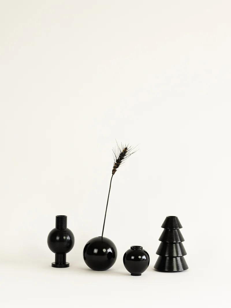 Four black geometric vases of different shapes and sizes are set against a light background. One holds a dried wheat stalk, adding a natural touch to the modern display, reflecting Titirangi’s woodturning craftsmanship.