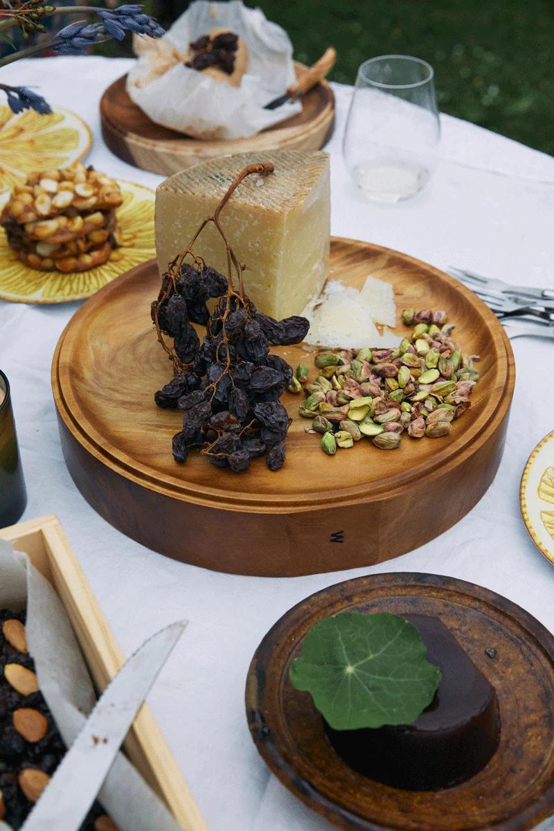 Cheese platter on white tablecloth. Christmas cake, wine glass, and outdoor dining setting visible.