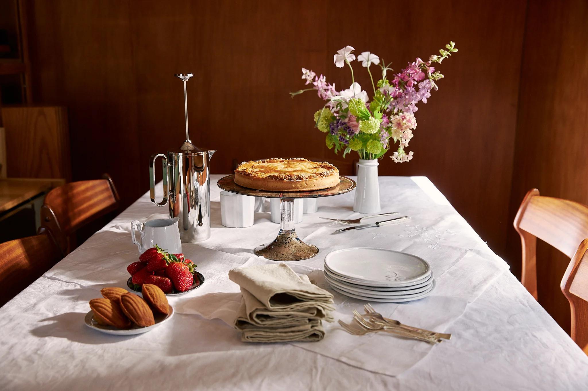 A wide shot of a table set in white cotton tablecloth and a complete spread of cake and coffee