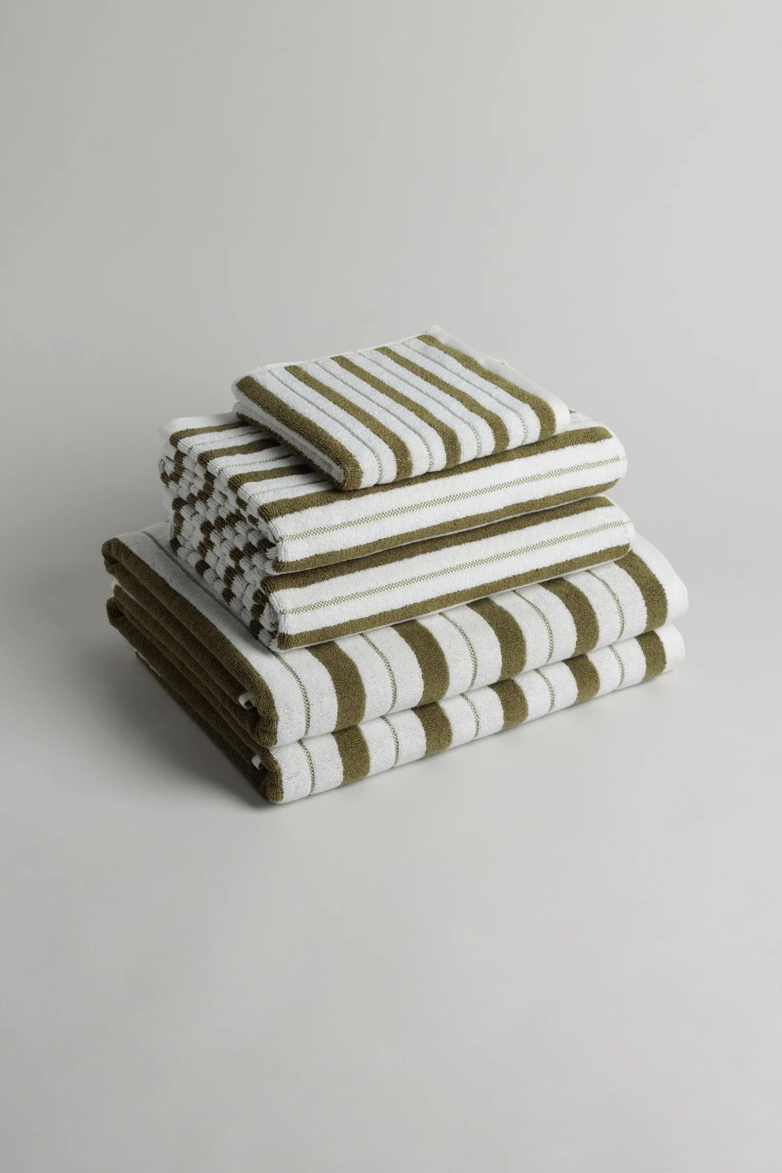 Folded stack of green and white striped towels against off-white background.