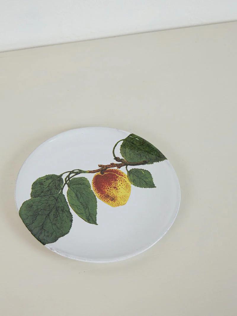 White plate with lemon design and green leaves. Spring flowers around edge. Rests on light-coloured surface.