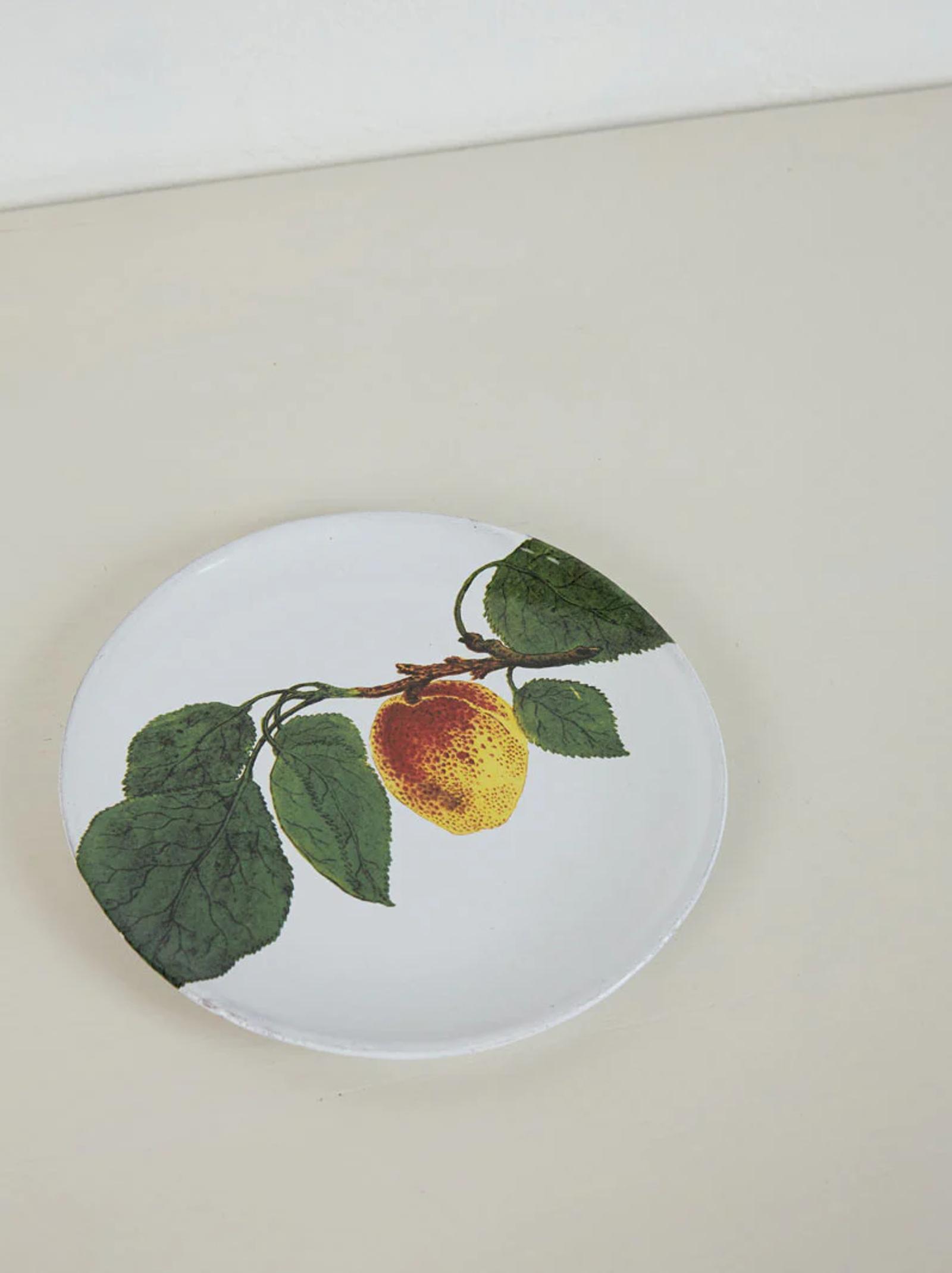White plate with lemon design and green leaves. Spring flowers around edge. Rests on light-coloured surface.