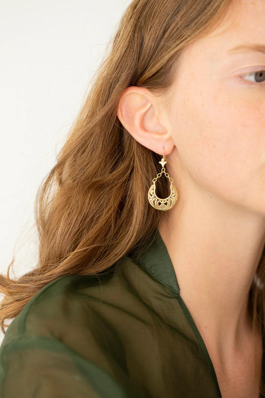 Person with light brown hair wearing gold crescent earring by Charlotte Penman. Green translucent top. Light background evokes elegant, magical mood.