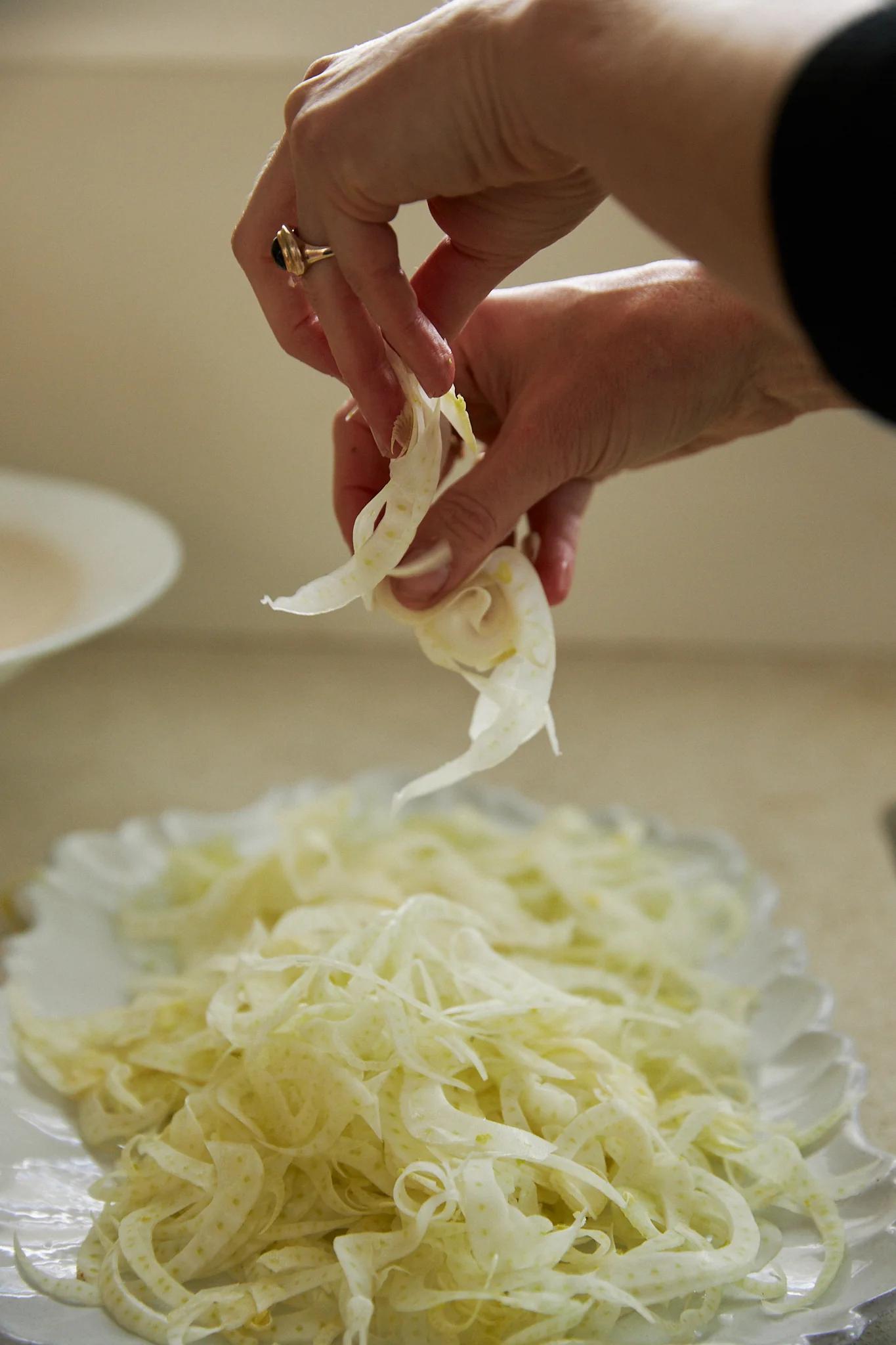 hands sprinkle finely sliced fennel over a platter