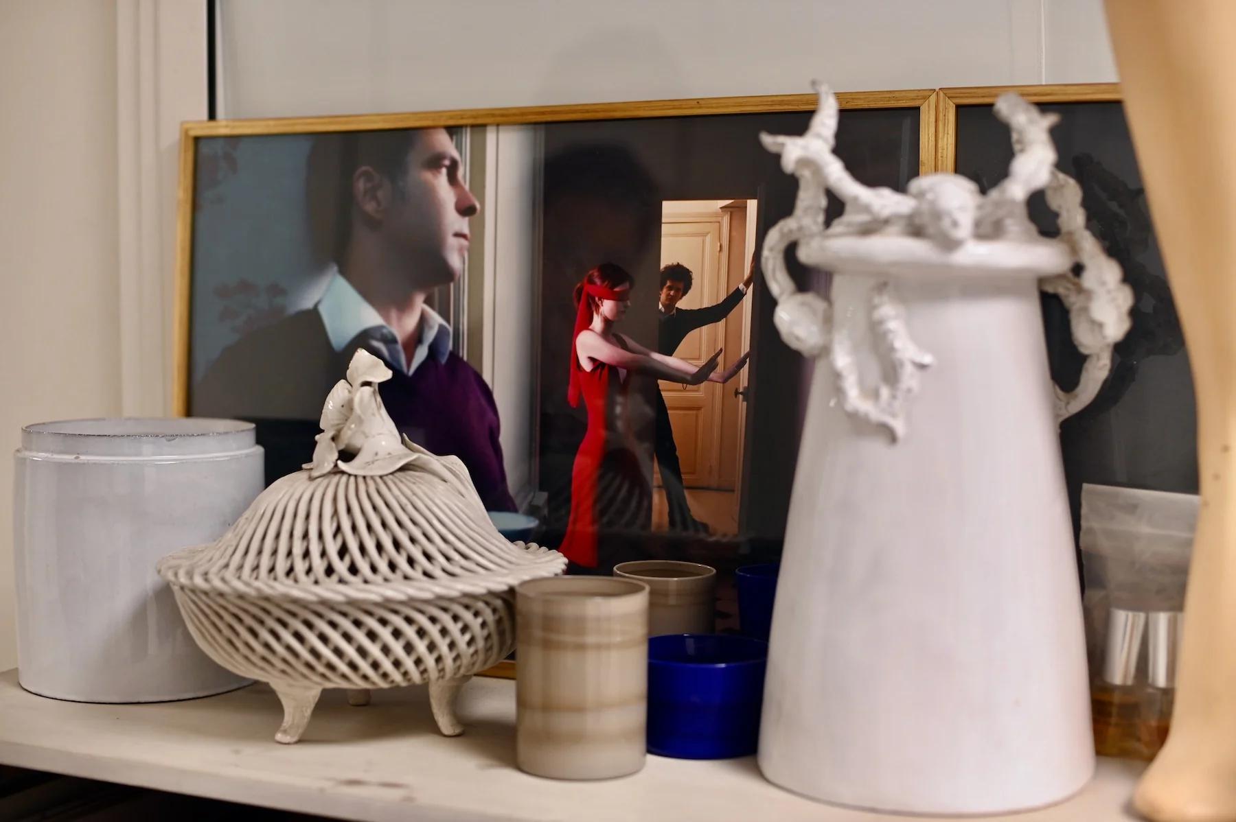 Shelf displays decorative items including white basket, candle, blue cups, and jug with intricate designs. Framed photo of dancing couple behind.