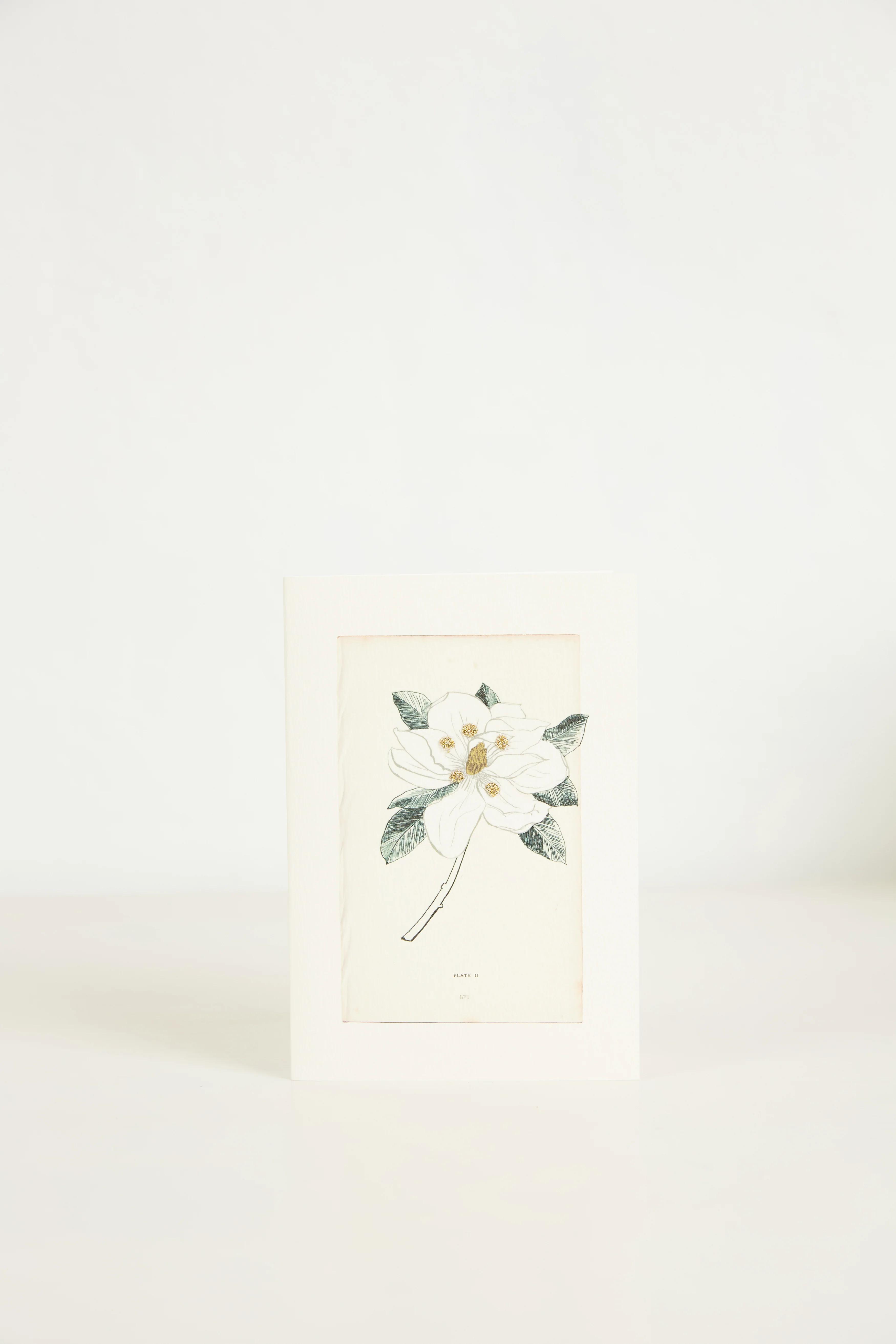 A minimalist greeting card with a hand-drawn white flower with green leaves. The card stands upright against a plain white background.