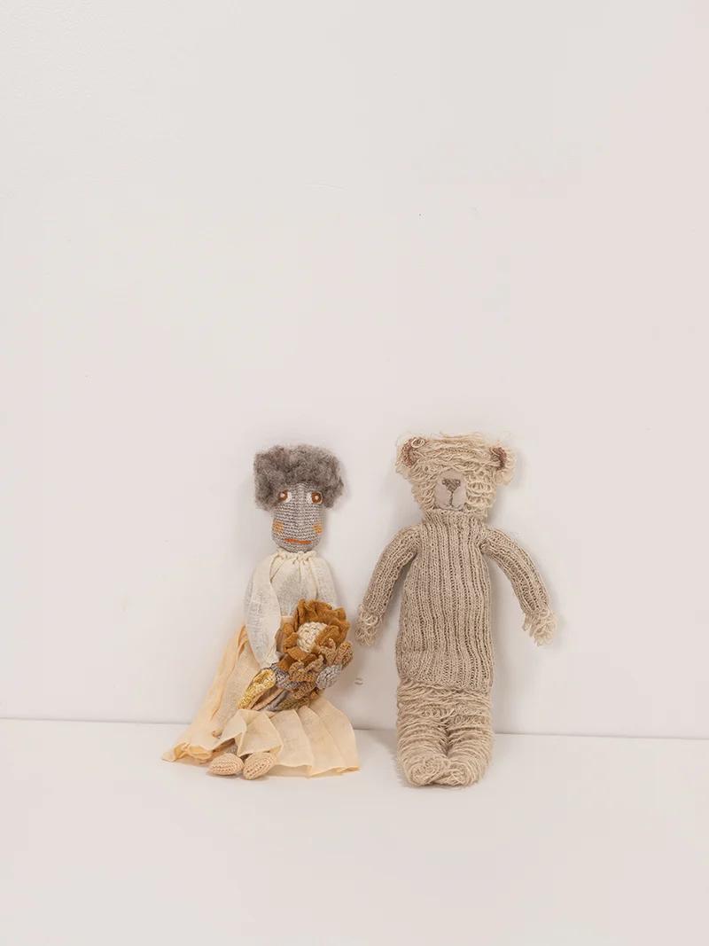 Two handcrafted dolls by Sophie Digard, one in an off-white dress holding a bear, the other resembling a beige bear with a textured body, against a white background.