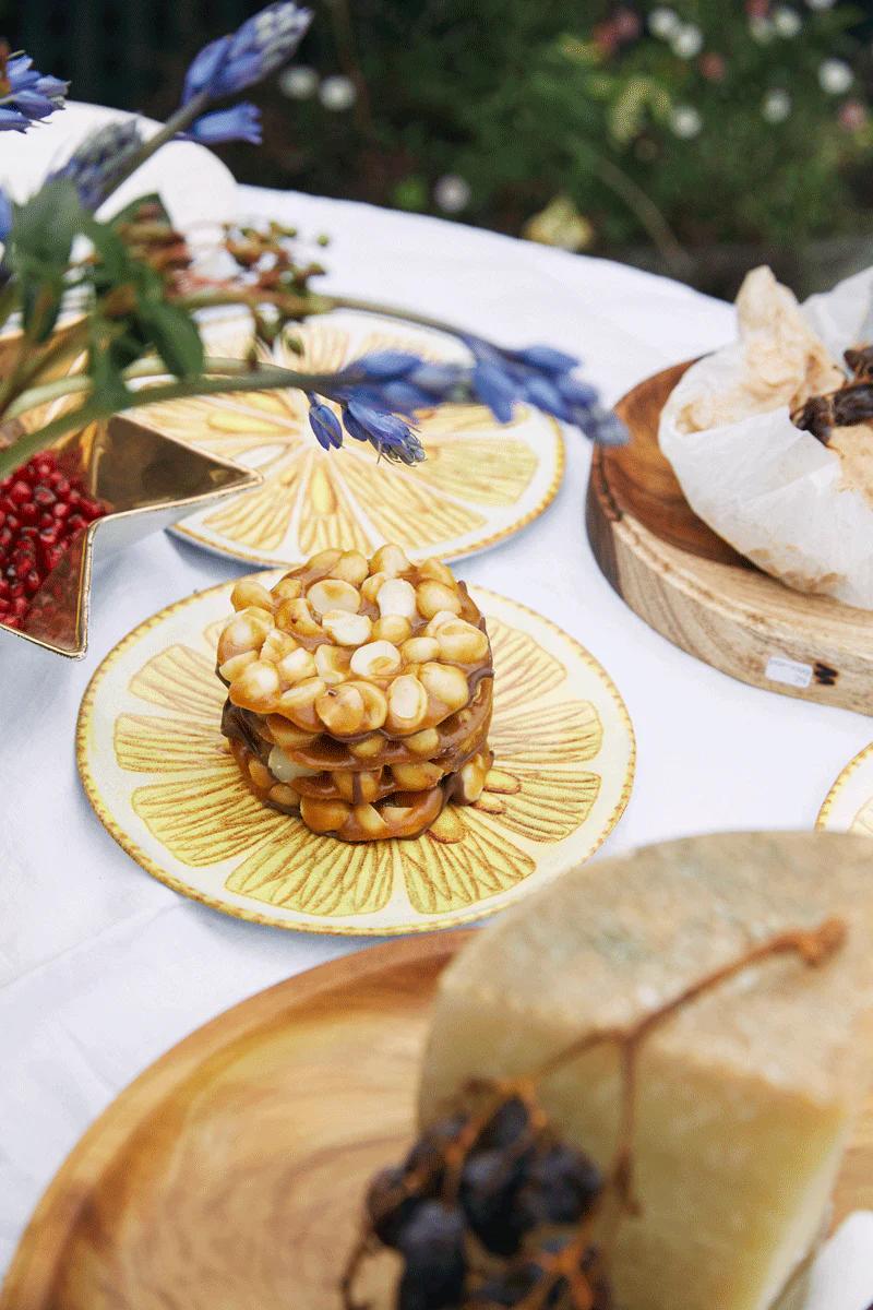 Outdoor table with Christmas cake, blue flowers, pomegranate seeds, and various dishes on white tablecloth.