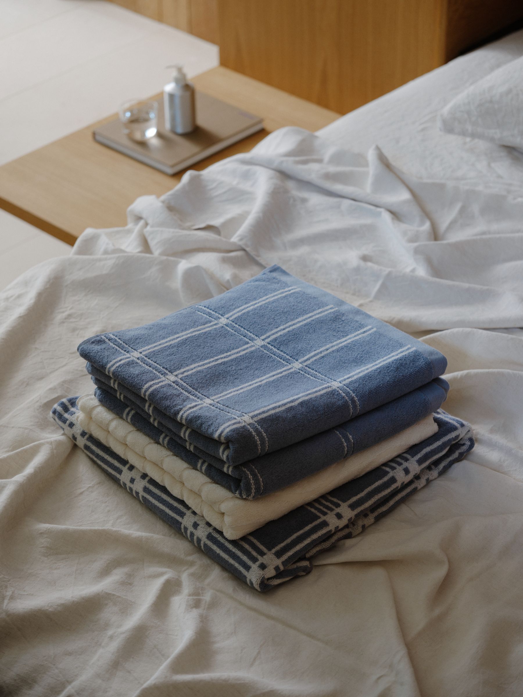 a stack of towels sitting on an unmade bed with wooden details