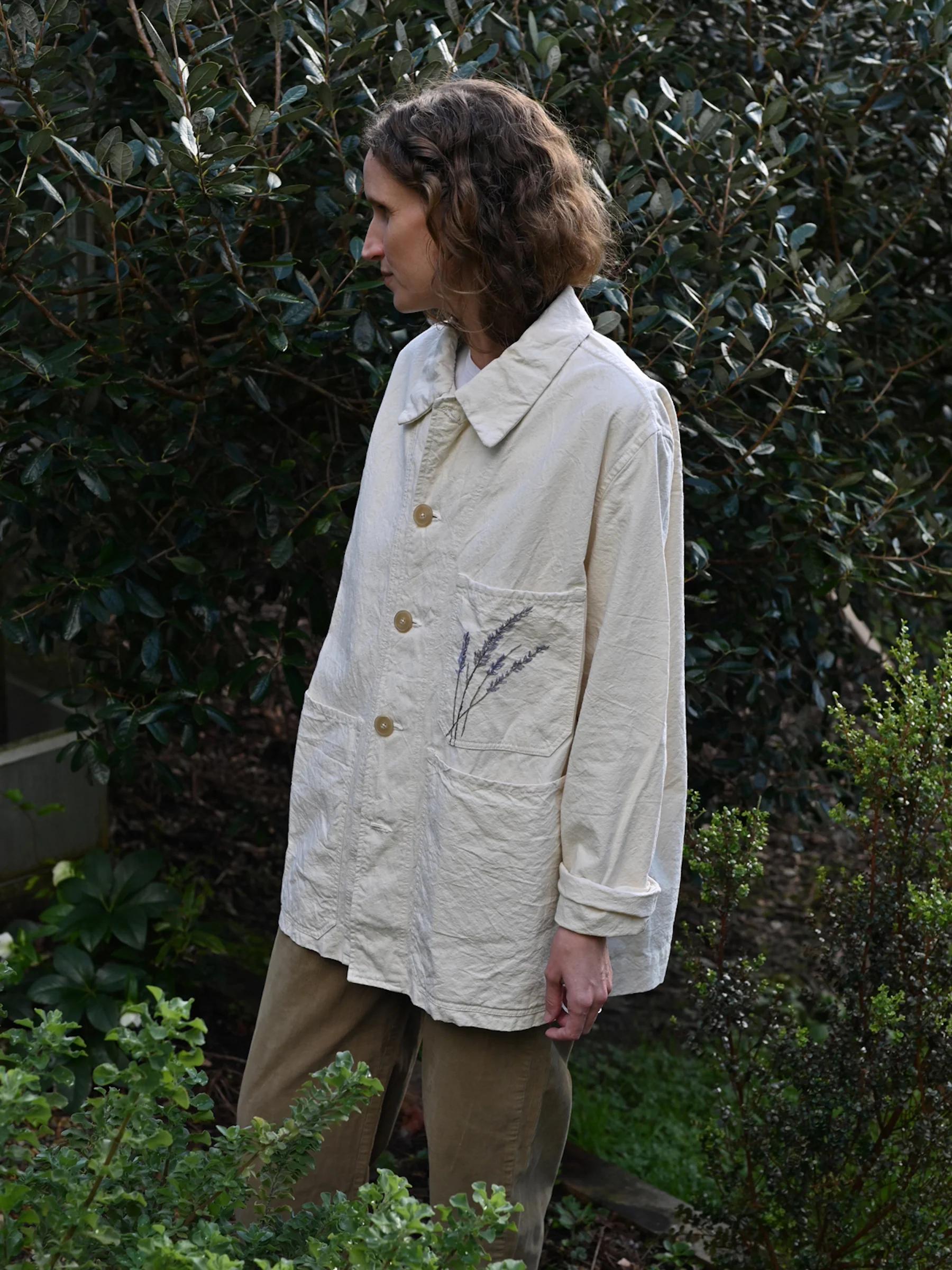 Oliver Church outdoors in light long-sleeve shirt and tan pants. Wavy hair, looking left. Greenery background showcases Singular Garments style.