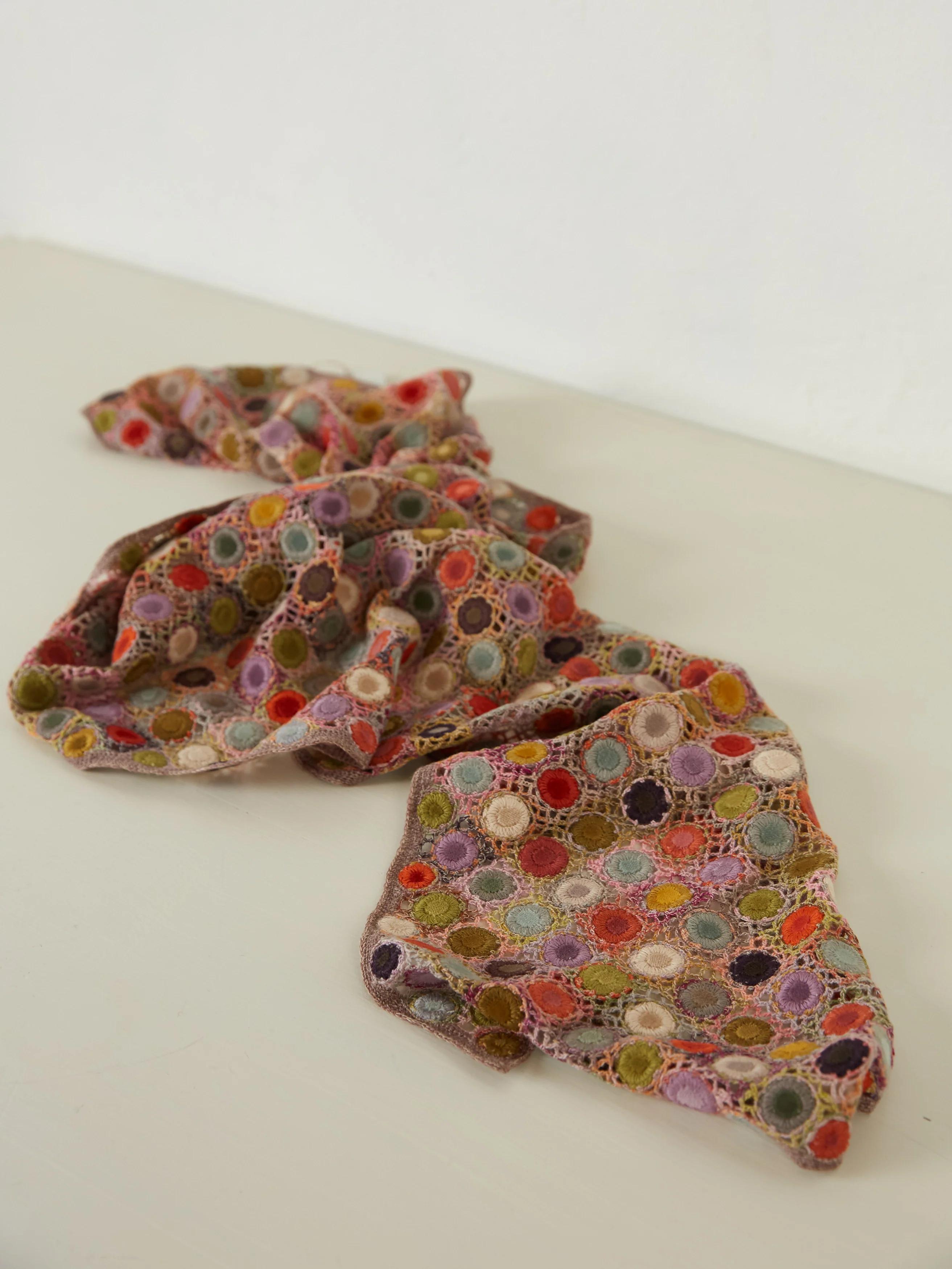 A colourful crocheted scarf by Sophie Digard with multicoloured circular motifs, spread out on a light surface.