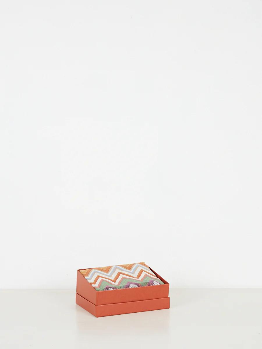 Open orange box revealing chevron fabric. Orange, white, green, pink, brown design. White background.