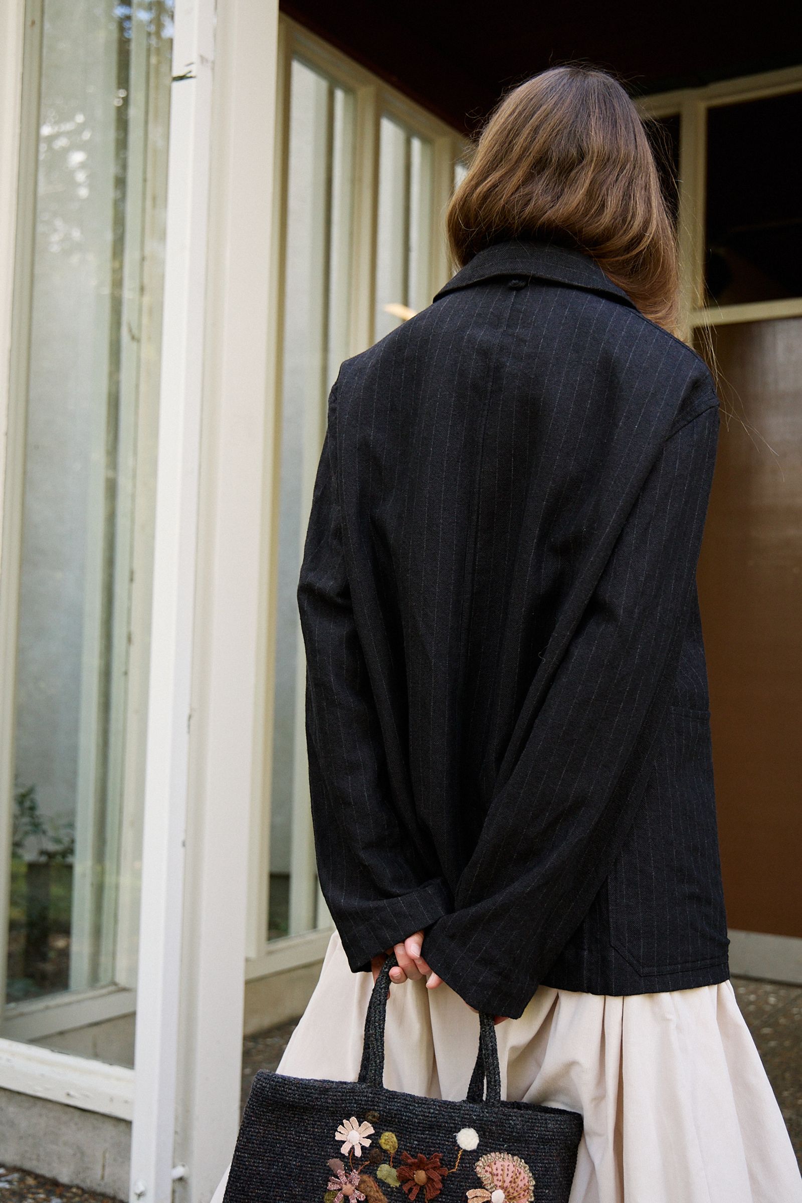 back of black jacket hands behind waist holding tote bag handles