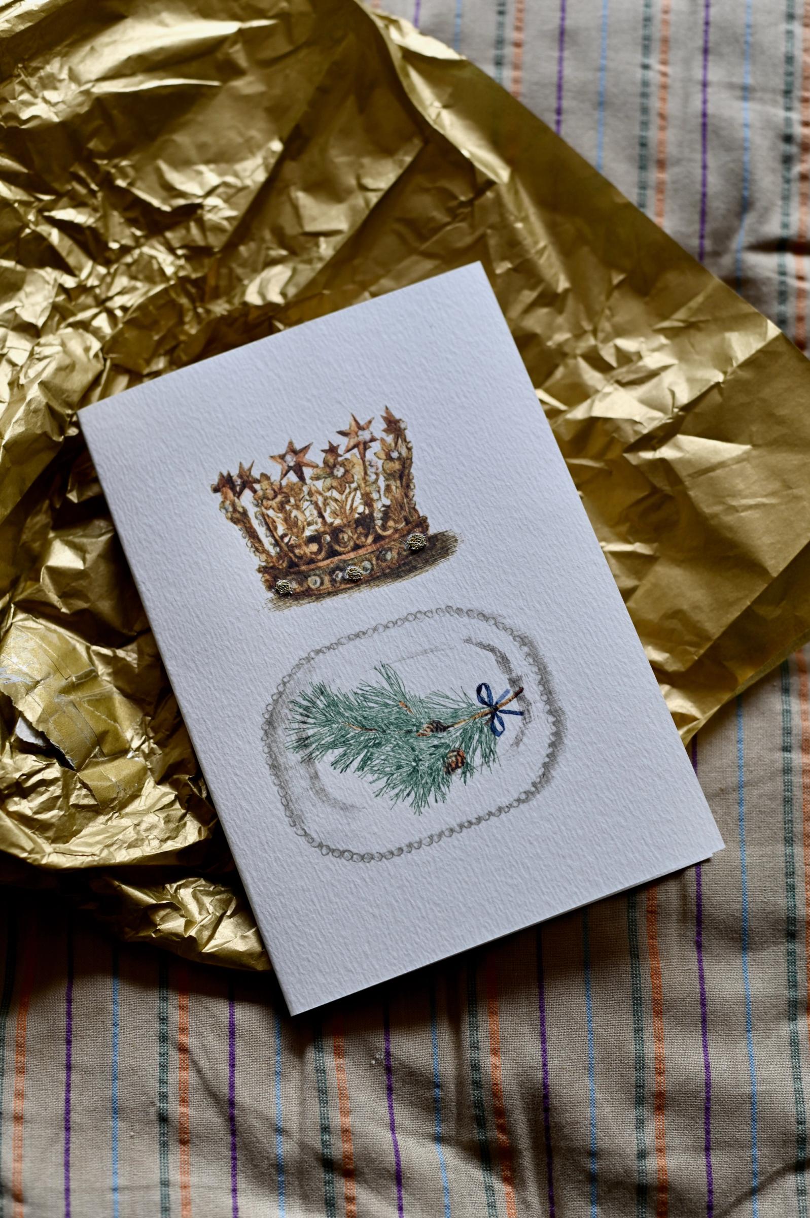 A greeting card with a antique crown stands upright against a plain, white background. The trees drawn are bare or with light foliage.