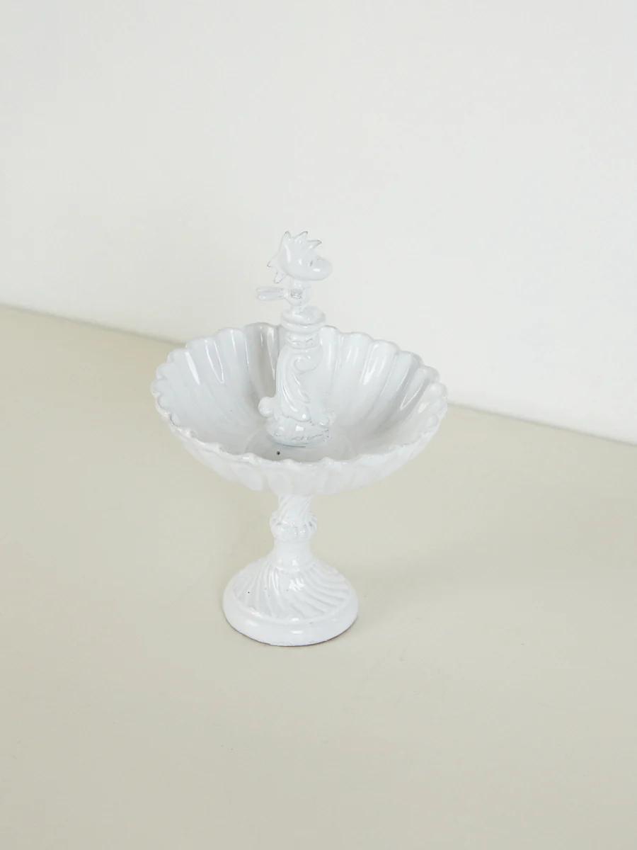 White ceramic bowl with scalloped edge, ornate stem, bird on top. Pedestal base. Light, plain background.