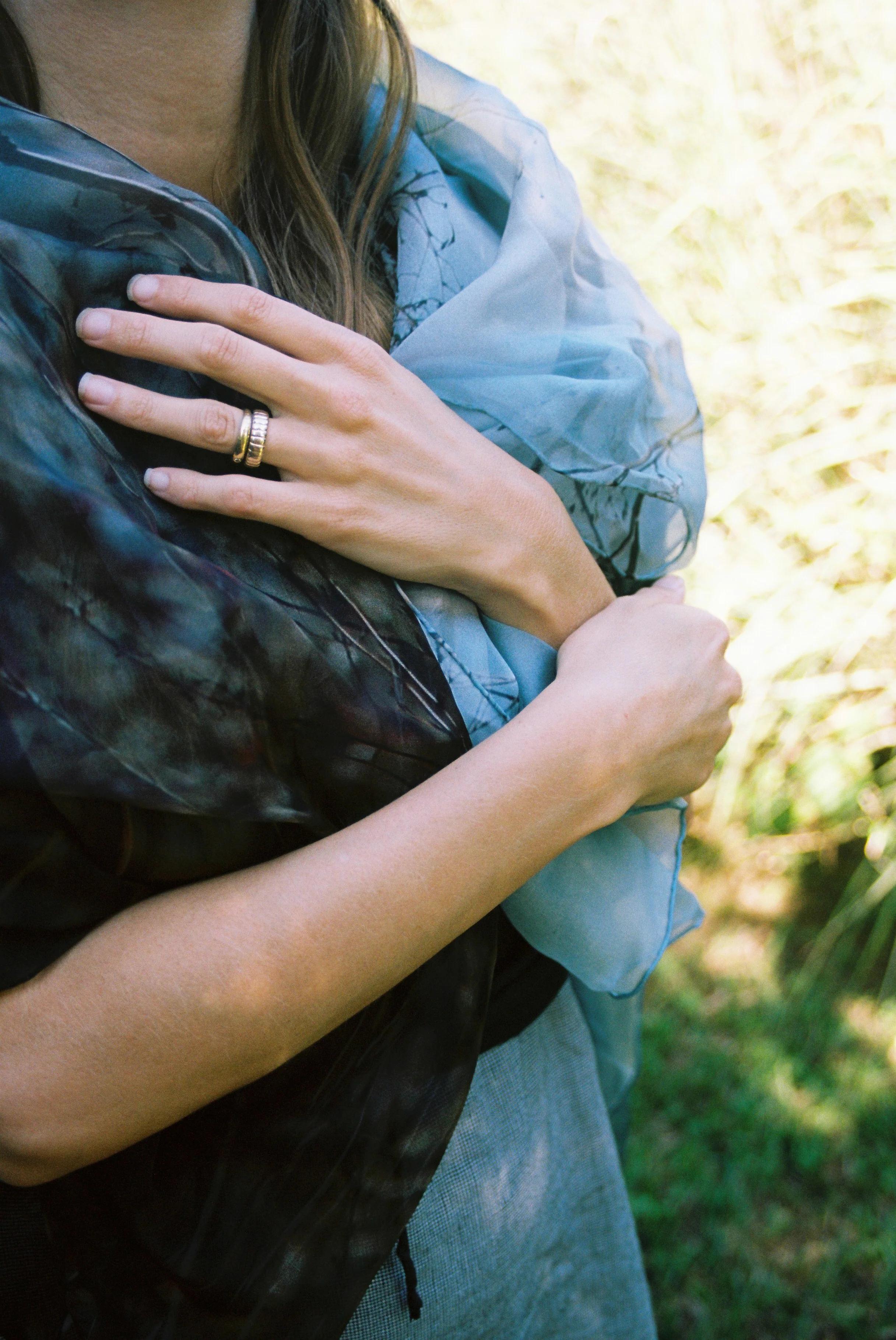 Person's shoulders and hands holding blue-brown patterned scarf. Gold ring visible. Green background.